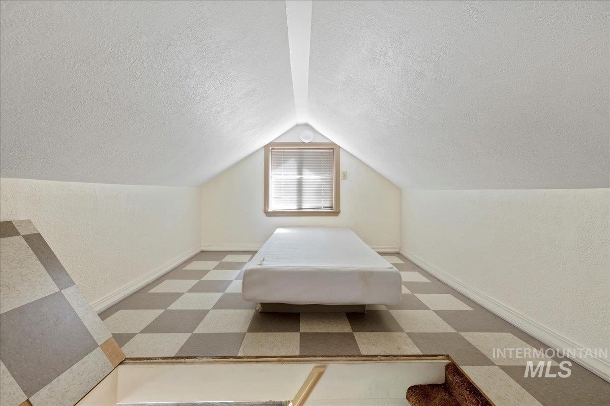 Unfurnished bedroom featuring a textured ceiling, vaulted ceiling, light flooring, and a textured wall