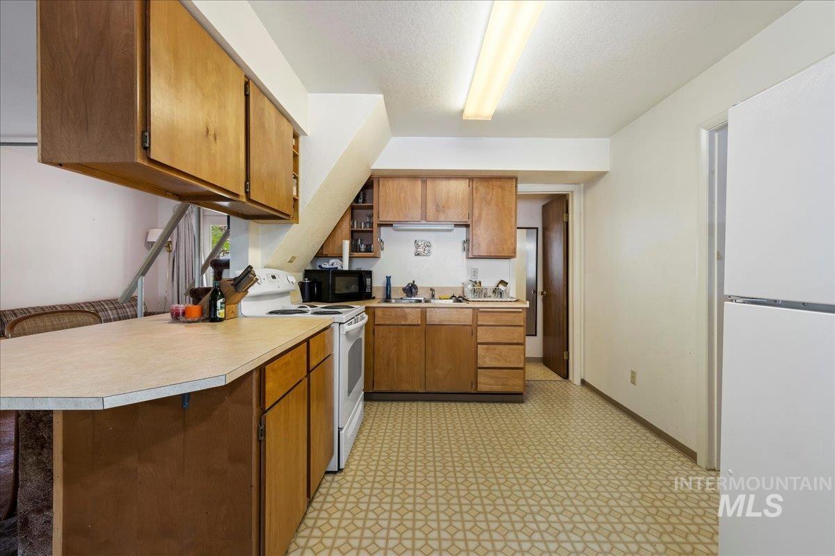Kitchen featuring white appliances, brown cabinets, light countertops, open shelves, and a textured ceiling