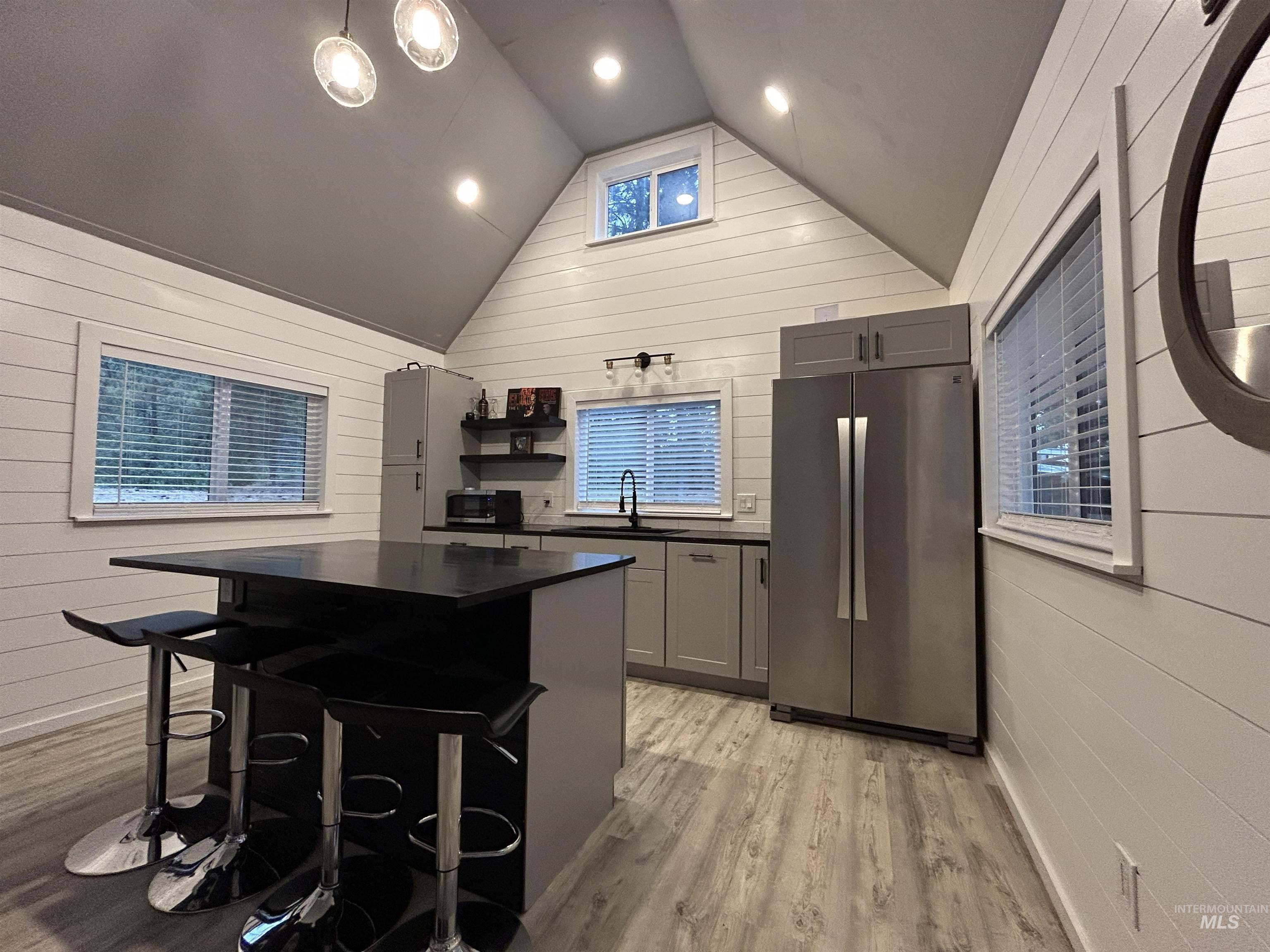 Kitchen featuring freestanding refrigerator, dark countertops, light wood-style floors, lofted ceiling, and gray cabinets