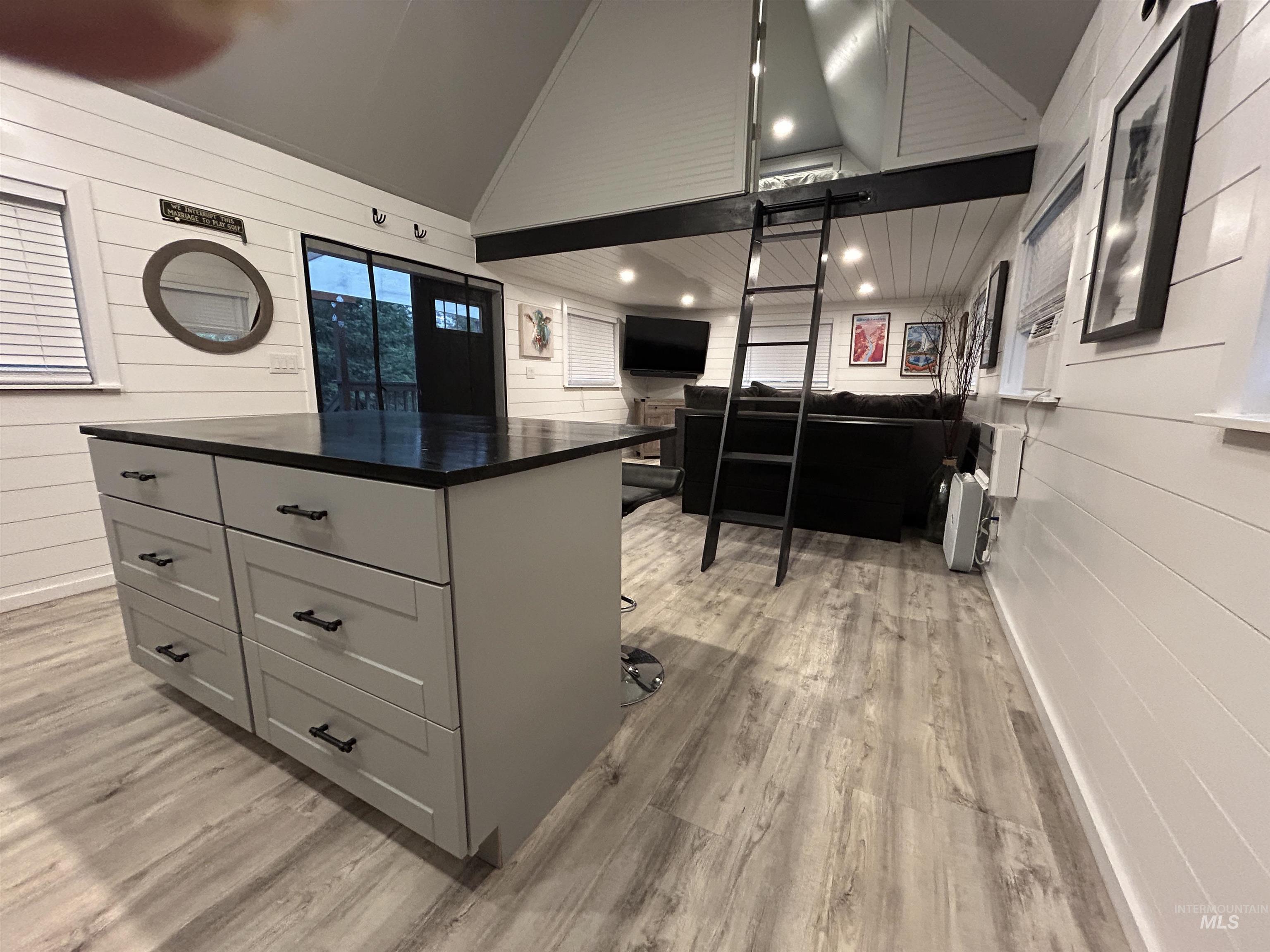 Kitchen featuring dark countertops, wood walls, gray cabinets, light wood finished floors, and a center island
