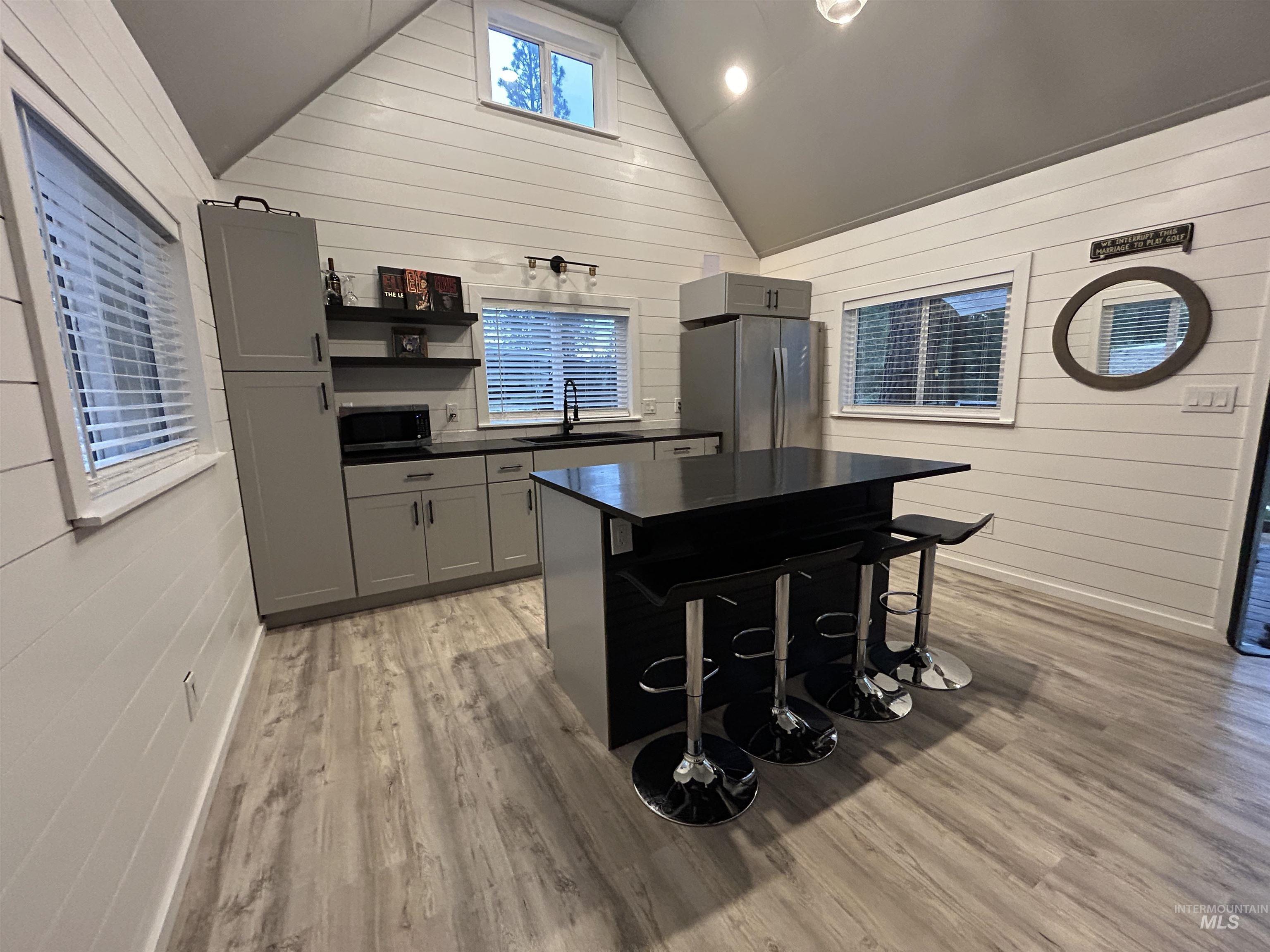 Kitchen featuring appliances with stainless steel finishes, dark countertops, wood walls, light wood-type flooring, and vaulted ceiling