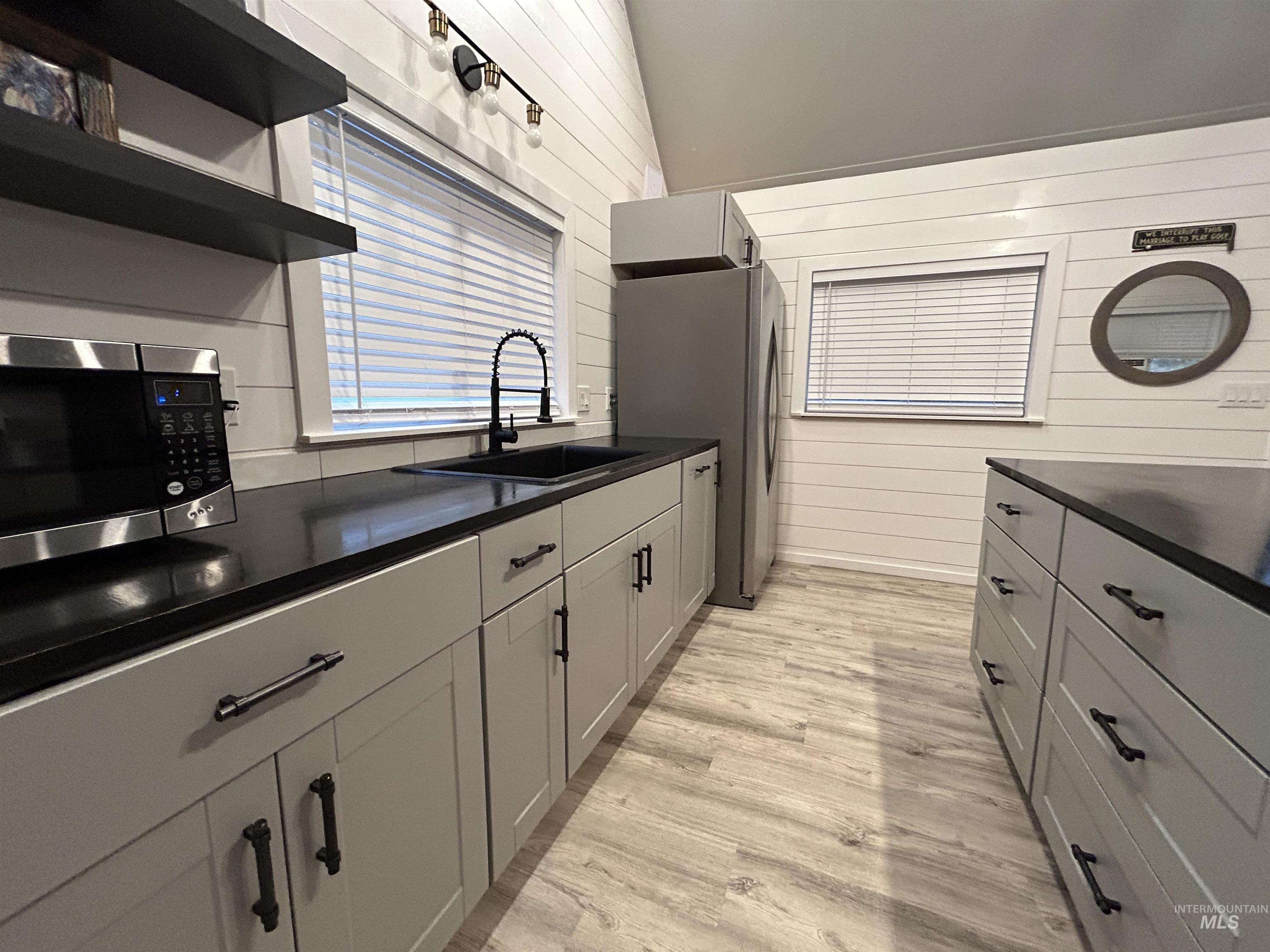 Kitchen with appliances with stainless steel finishes, dark countertops, light wood-style floors, and open shelves