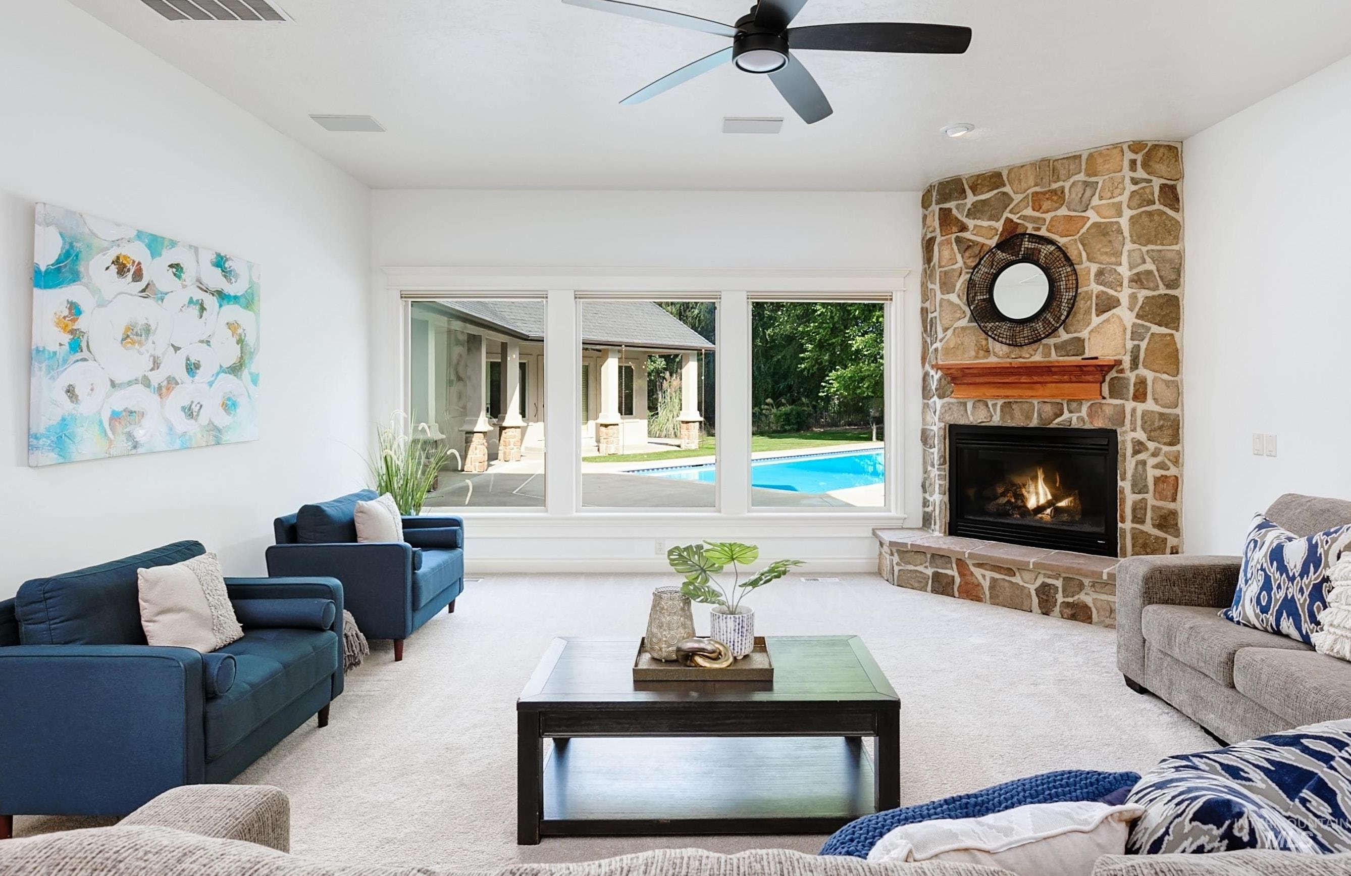 Carpeted living area with a stone fireplace and a ceiling fan