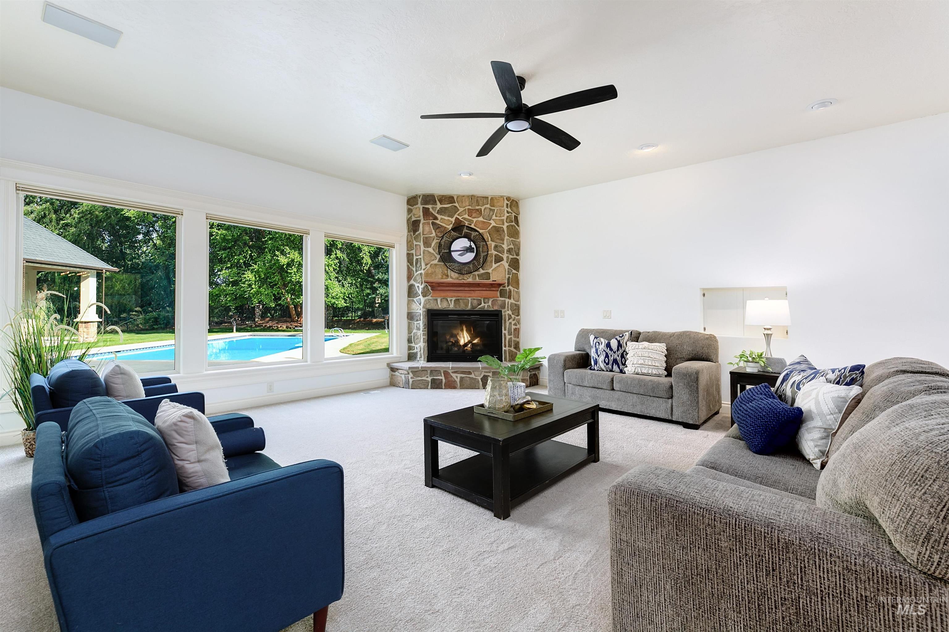 Carpeted living area with a stone fireplace and a ceiling fan