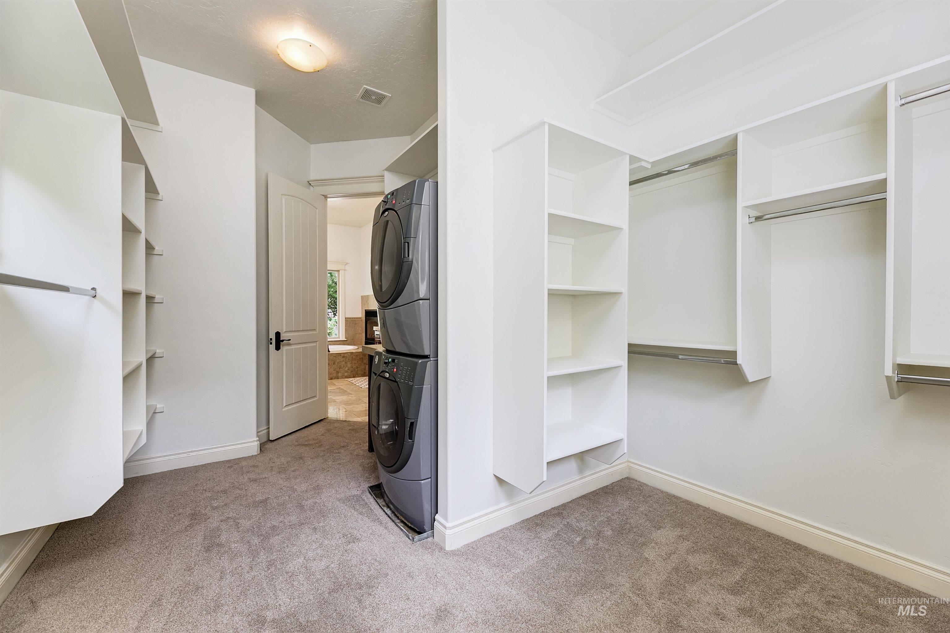 Walk in closet featuring light colored carpet and stacked washer and clothes dryer