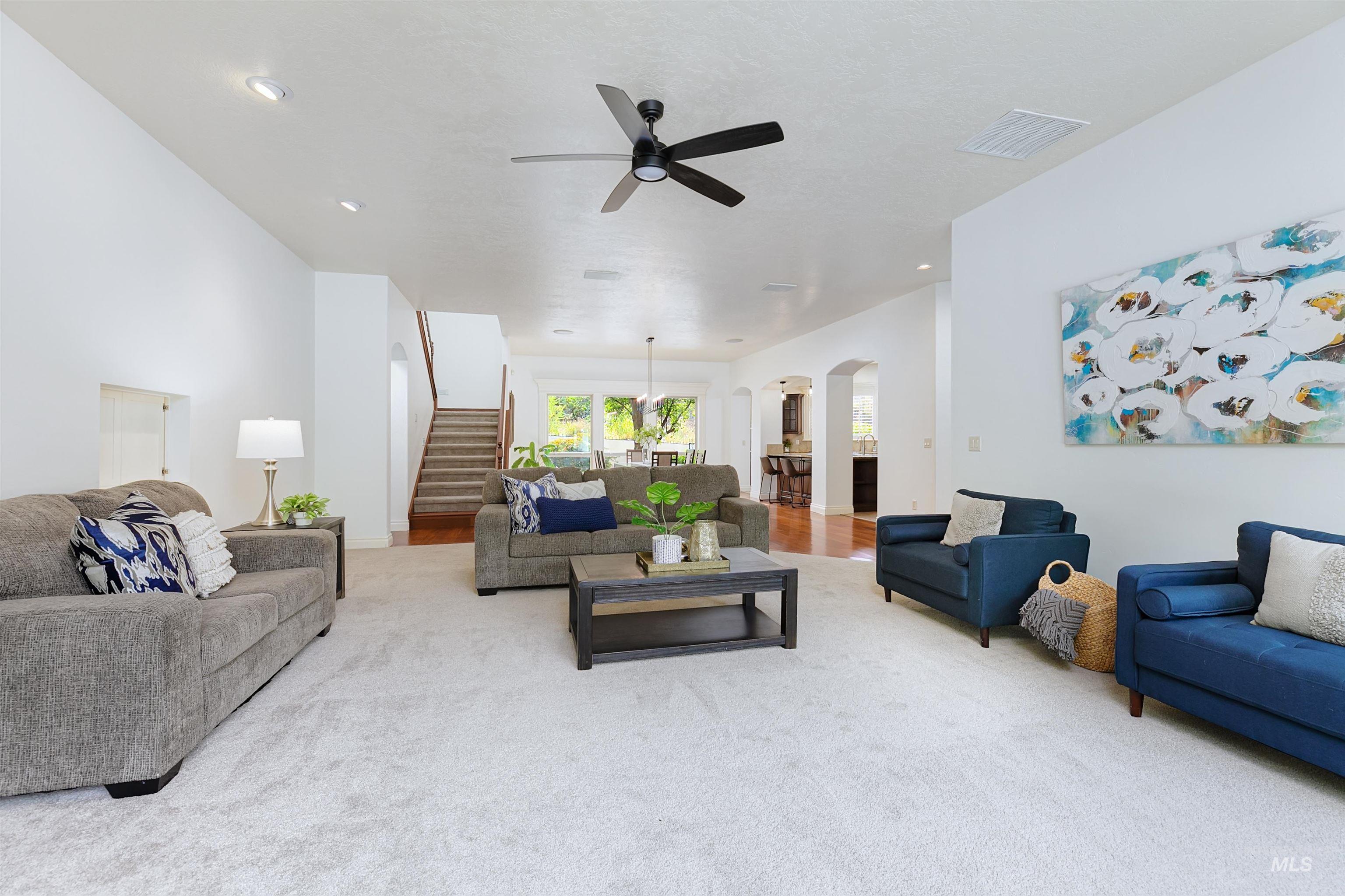 Living area with arched walkways, carpet, and a ceiling fan