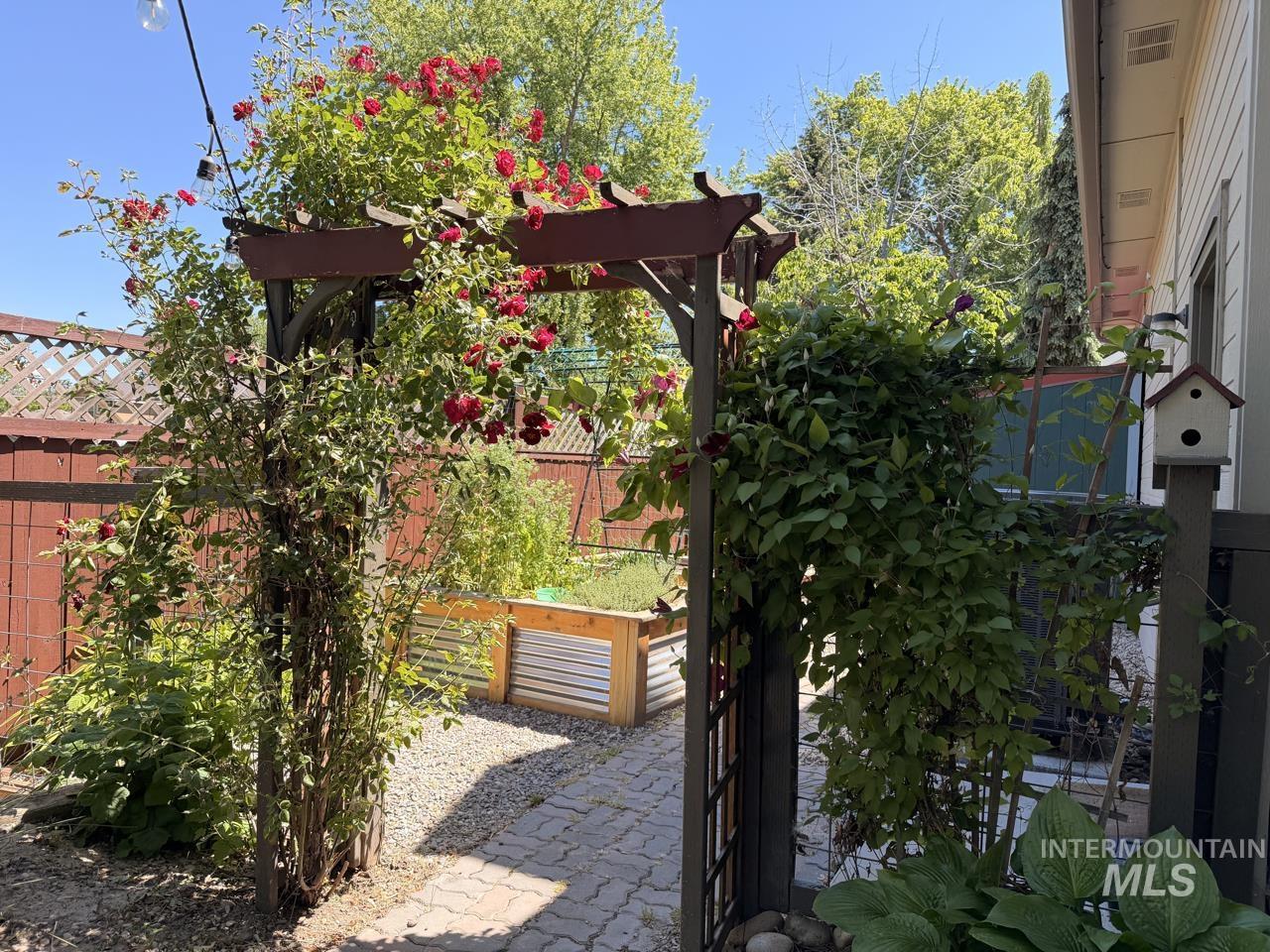 Garden arbor entry featuring climbing roses, brick paver pathway, gravel landscaping, and raised garden beds