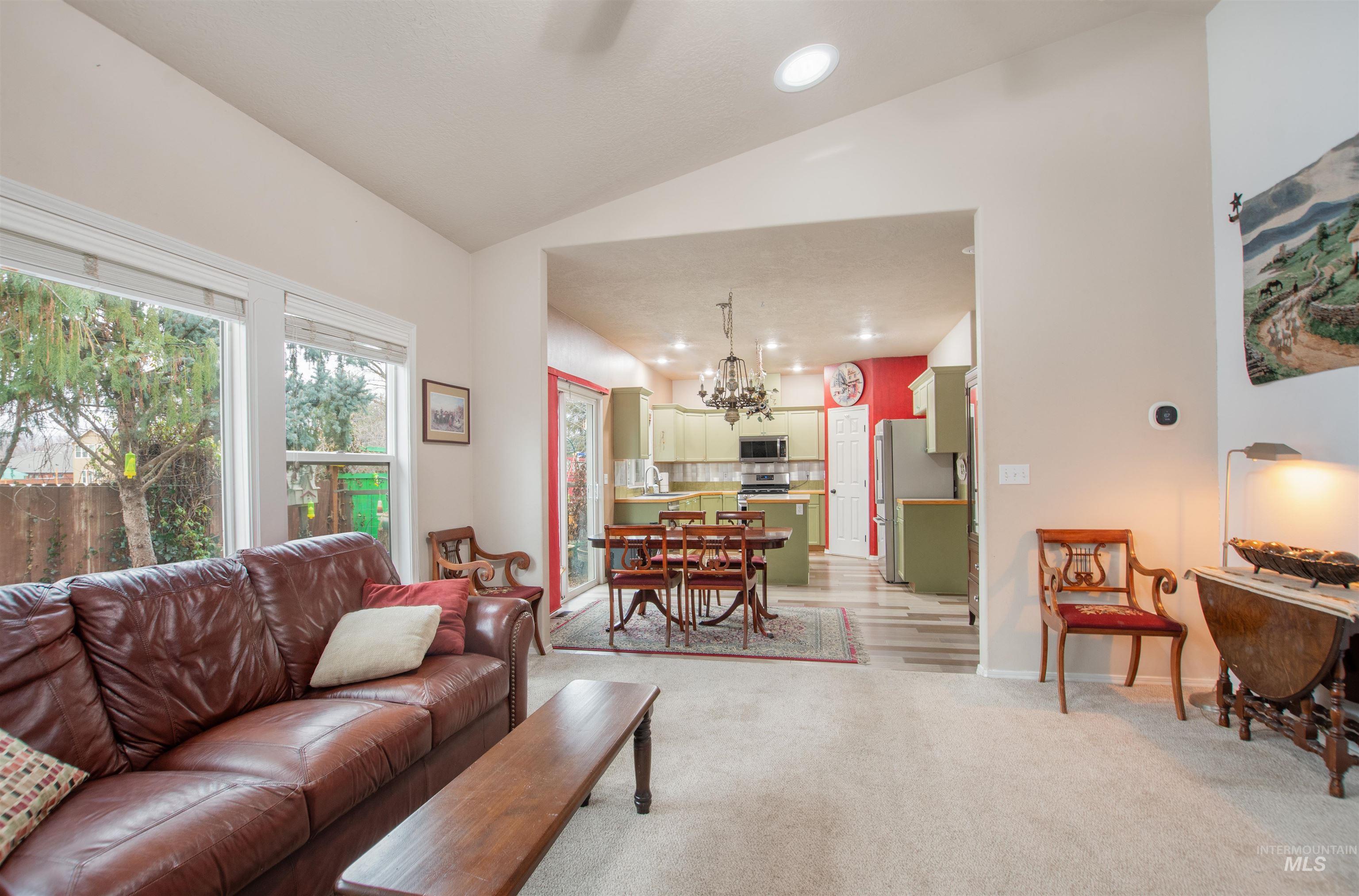 Living area with lofted ceiling, hanging lights, light colored carpet, and a ceiling fan