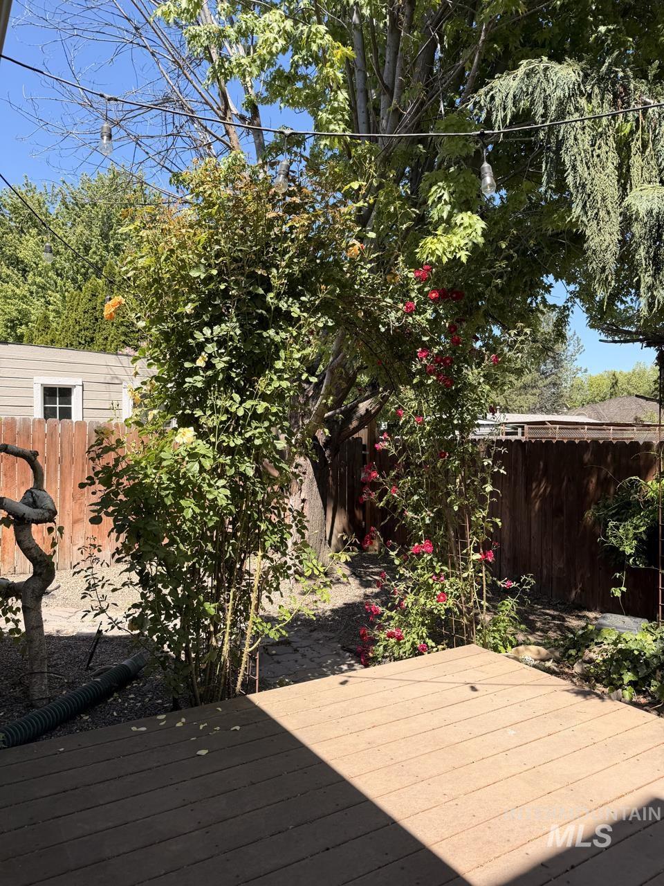 Outdoor deck space featuring composite decking, mature plantings, and a wood fence border