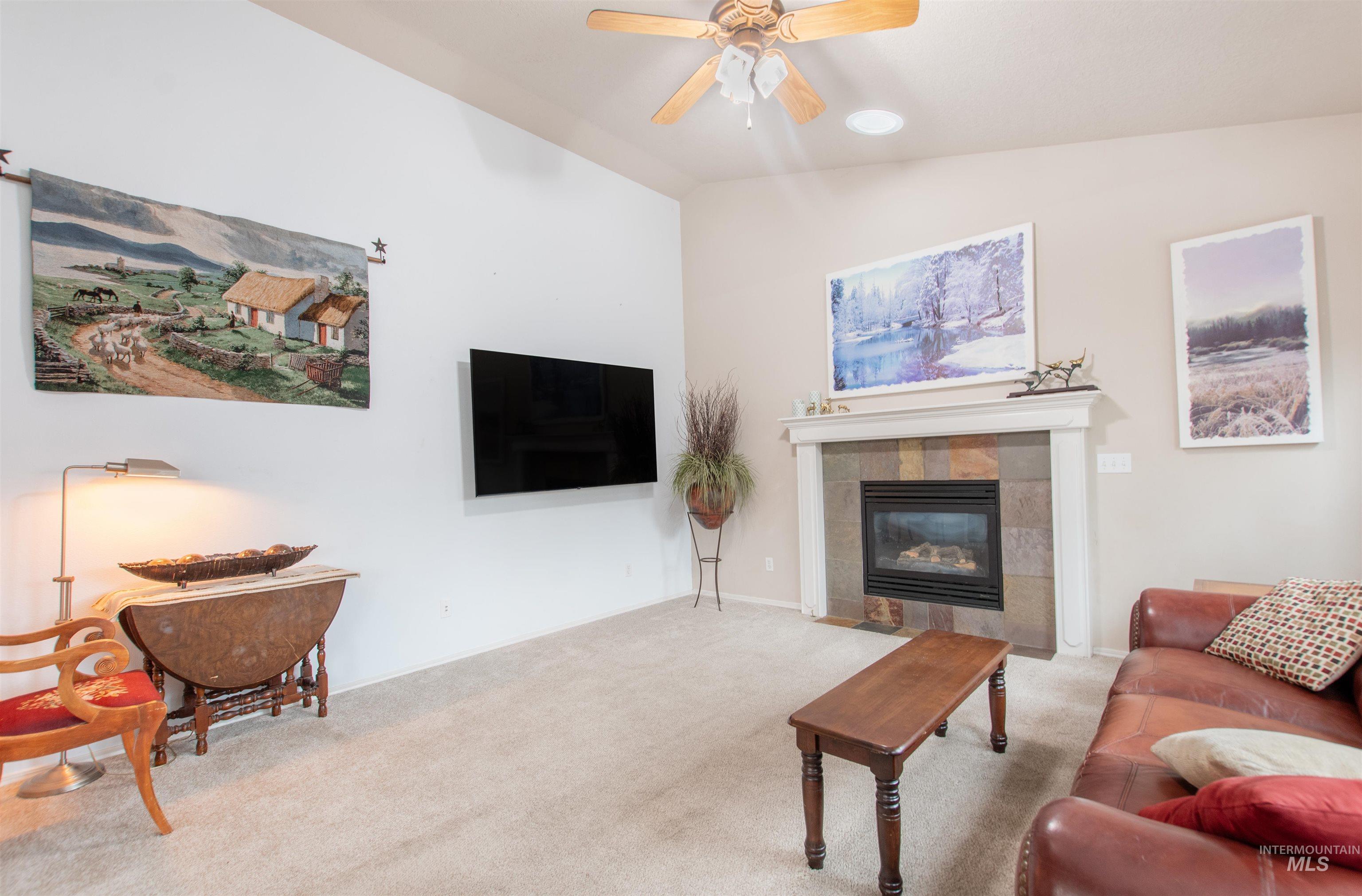 Carpeted living room with ceiling fan, vaulted ceiling, and a fireplace