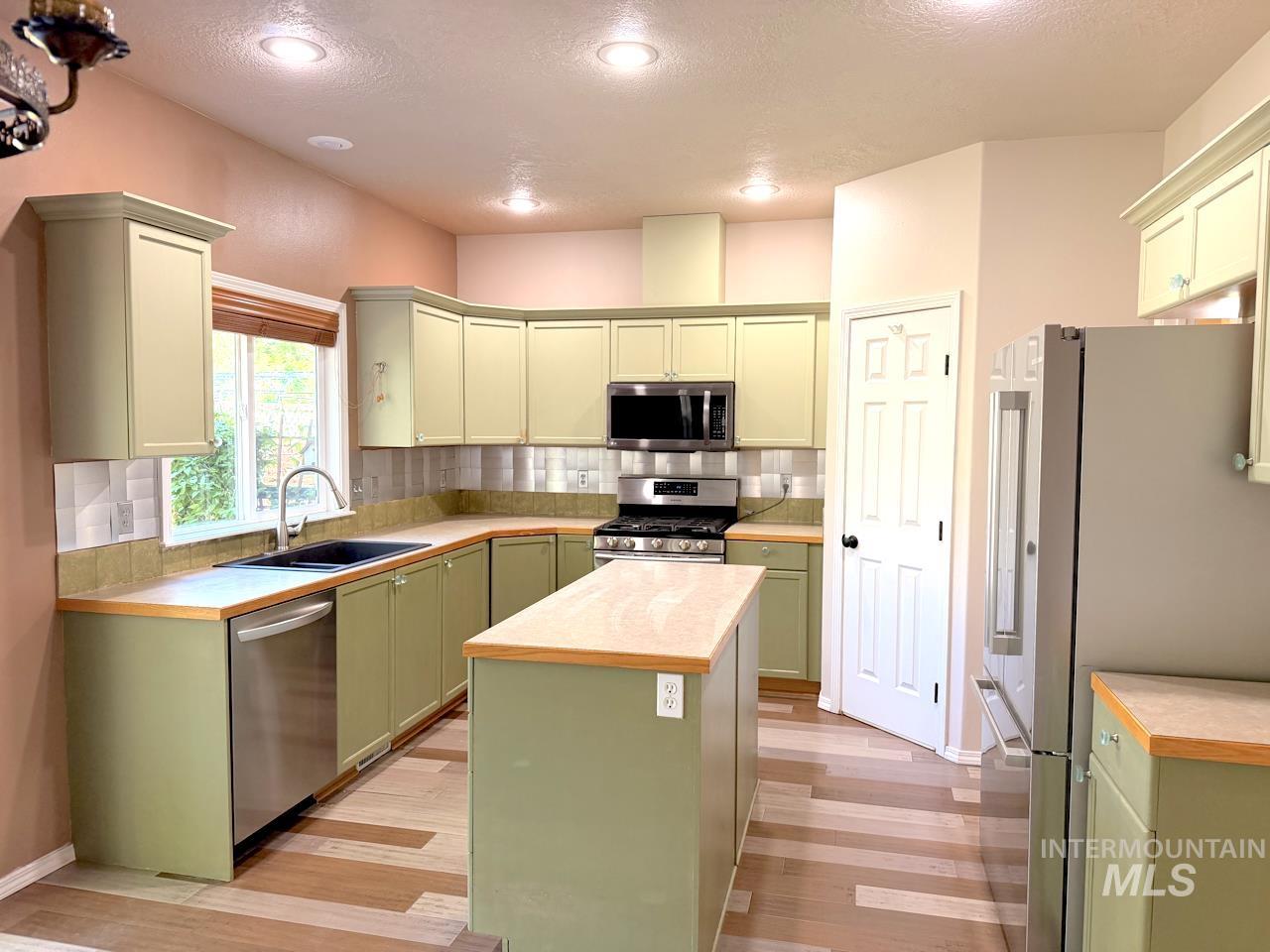 Kitchen featuring extensive cabinetry in a muted green finish, light wood-finish countertops, and a central island