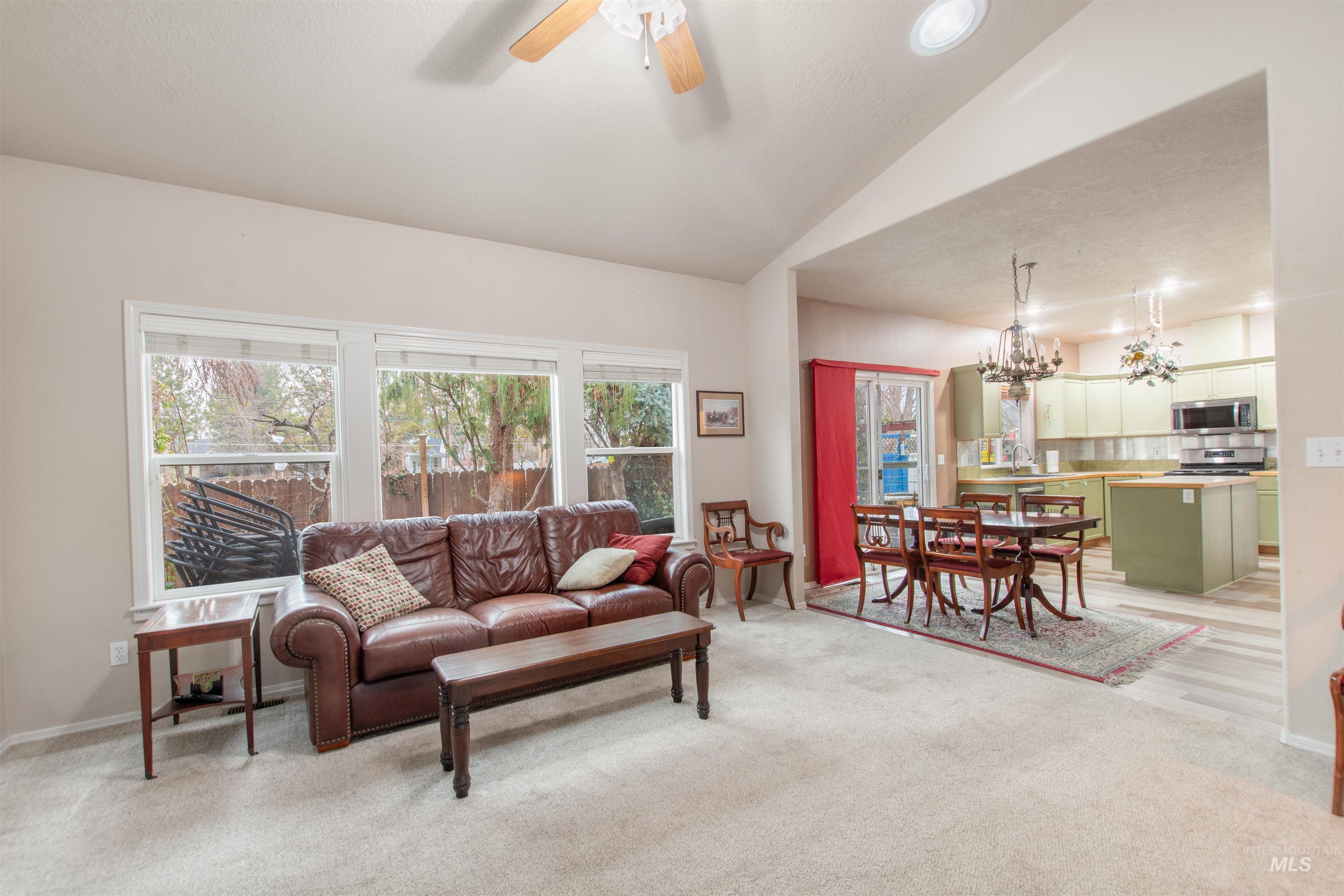 Living room with a ceiling fan, lofted ceiling, light carpet, and hanging lights