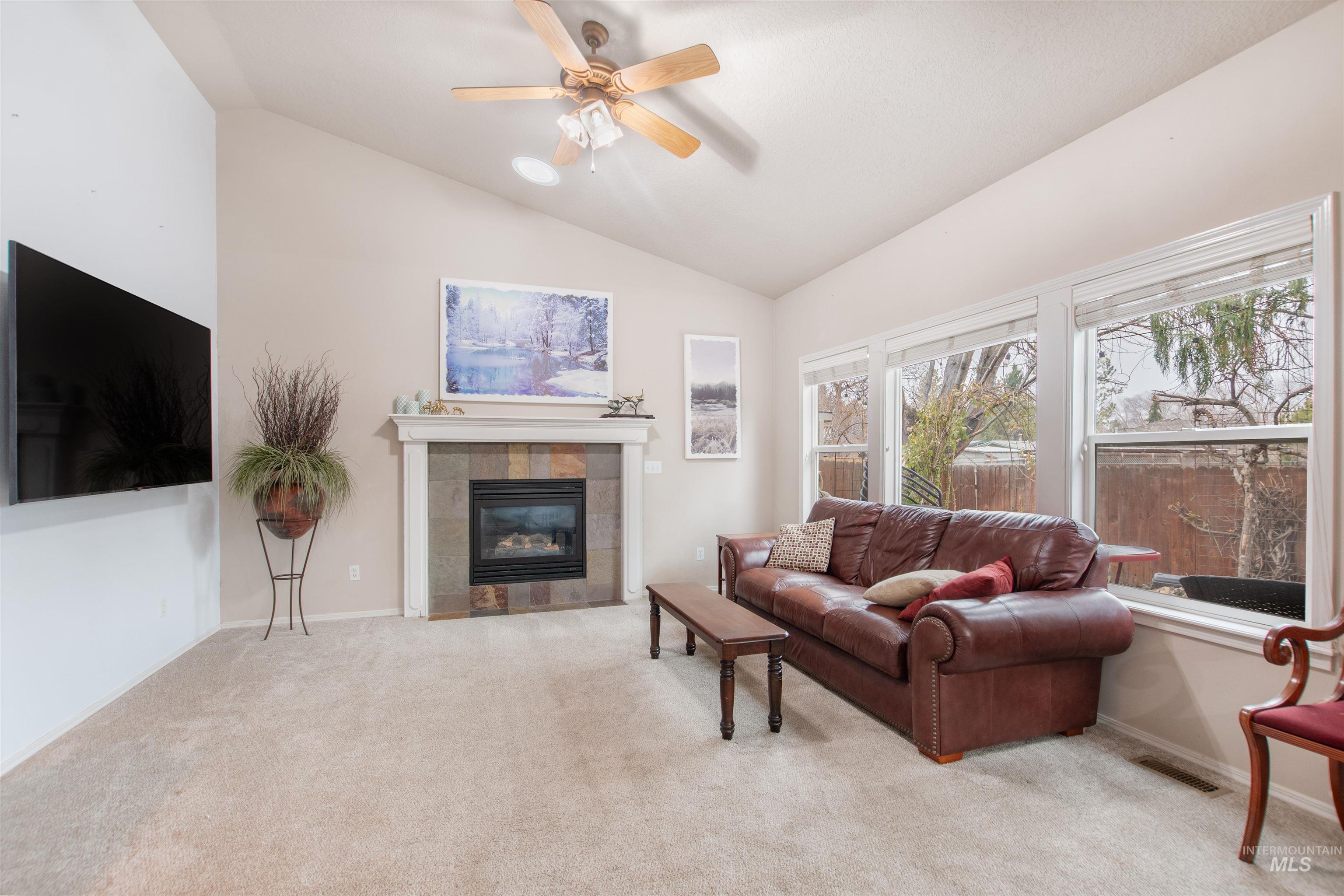 Living area featuring lofted ceiling, ceiling fan, light carpet, and a fireplace