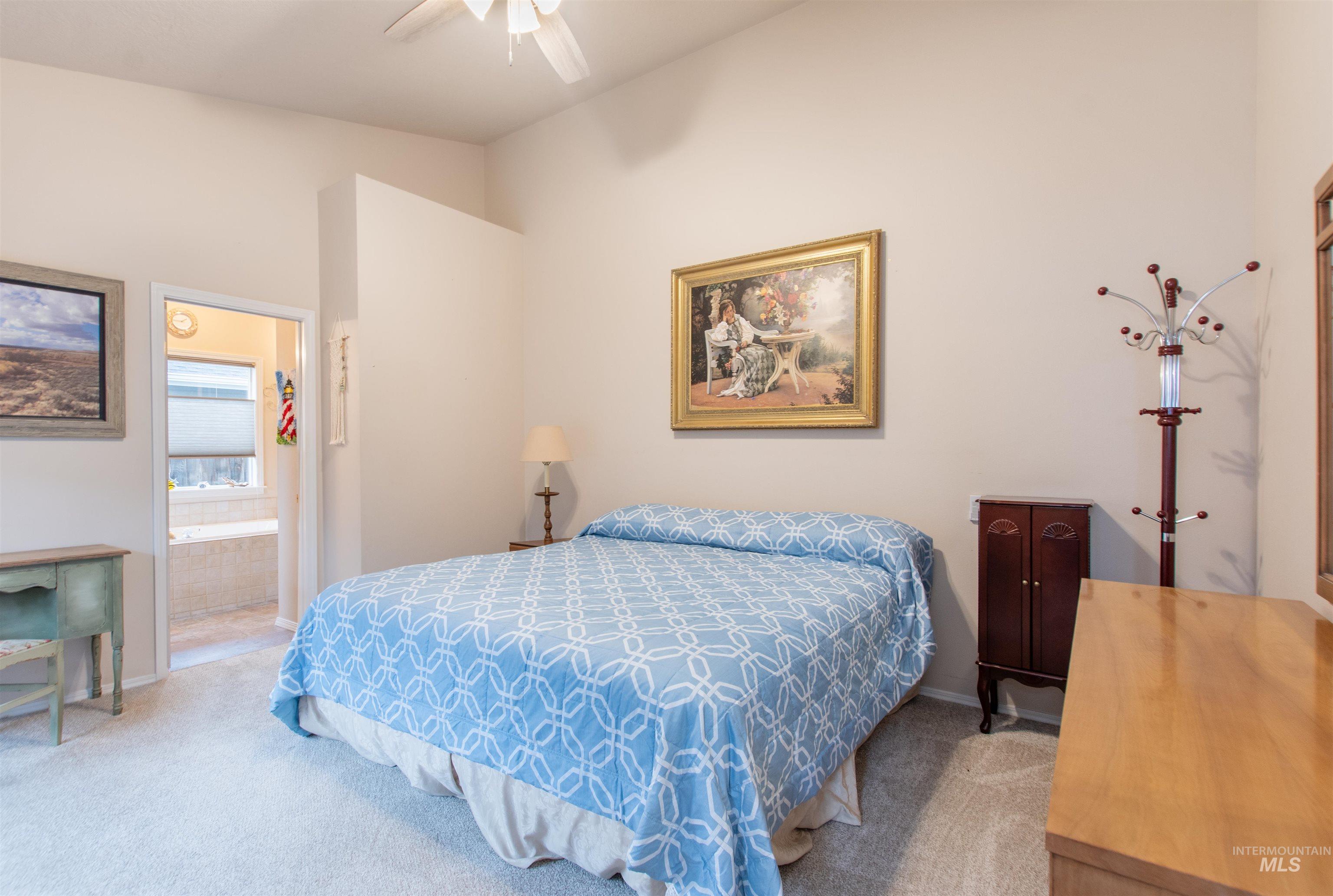 Bedroom with connected bathroom, light carpet, ceiling fan, and vaulted ceiling
