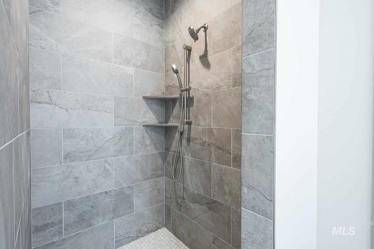Tiled shower featuring light grey rectangular tiles, dual shower heads, and two built-in corner shelves