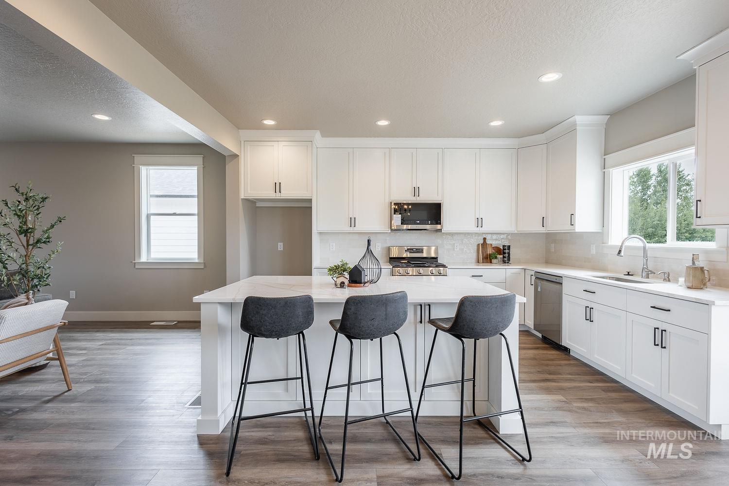 Spacious kitchen featuring white cabinetry, stainless steel appliances, a center island with seating, a white subway tile backsplash, and wood-finish flooring