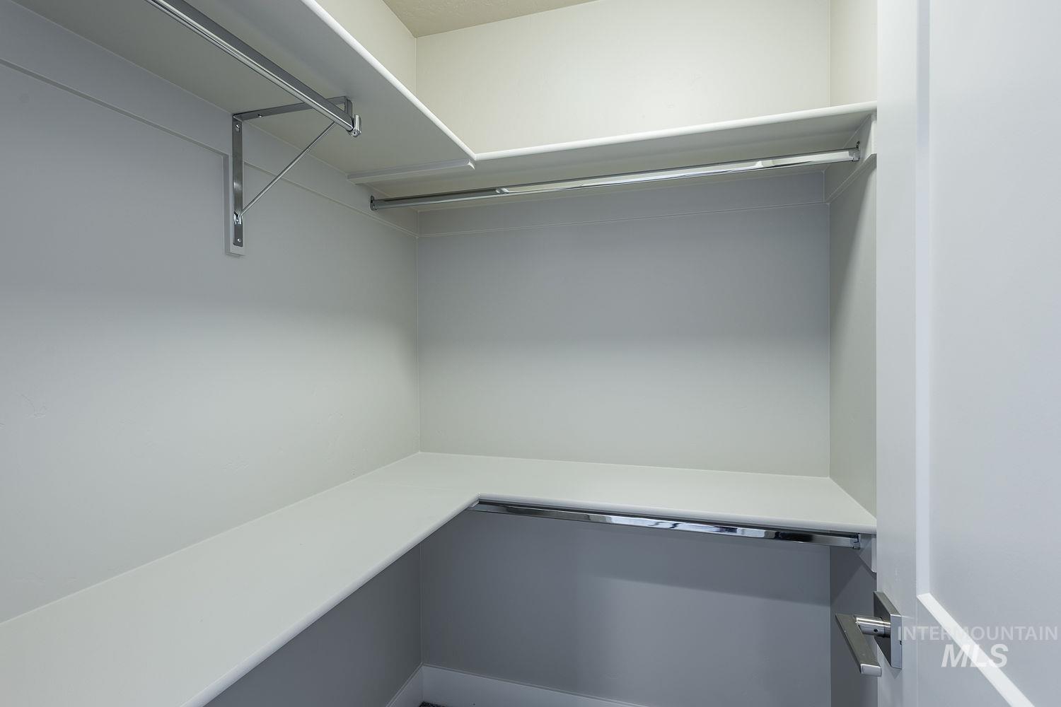 Walk-in closet featuring white shelving and chrome hanging rods