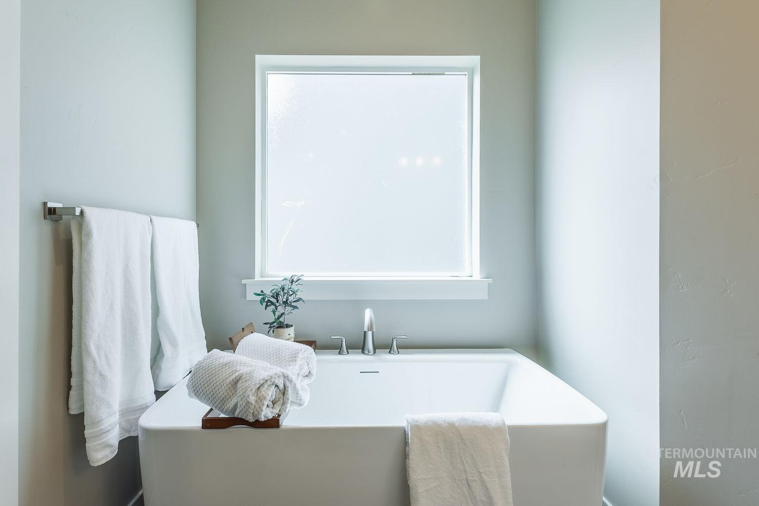 Freestanding soaking tub with a deck-mounted faucet and a frosted window