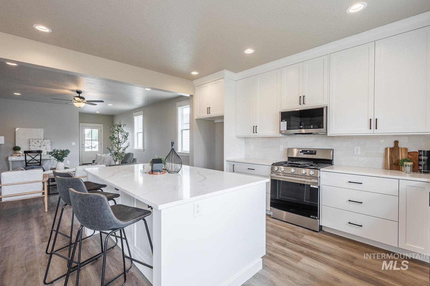 Kitchen featuring a large central island with a solid surface countertop, white cabinetry with black hardware, stainless steel range with overhead microwave, and wood-finish flooring