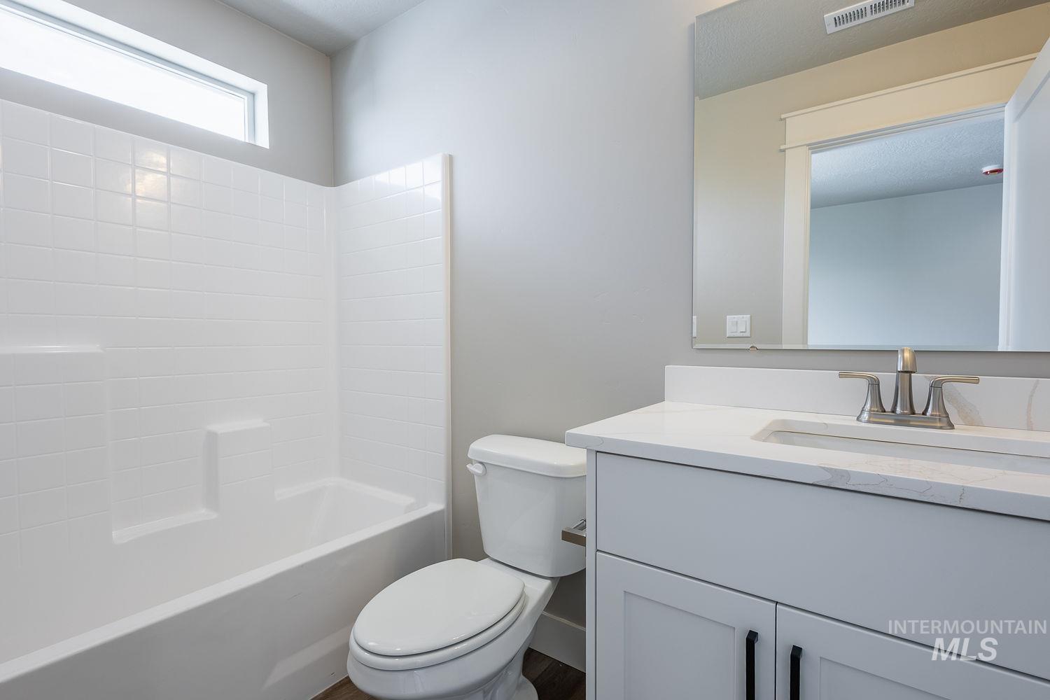 Bathroom featuring a white bathtub with subway tile surround, an overhead transom window, a white vanity with integrated sink, a large wall-mounted mirror, and brushed nickel fixtures