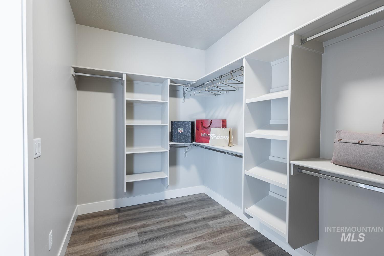 Walk-in closet featuring built-in shelving, multiple hanging rods, durable wood-finish flooring, and light gray walls