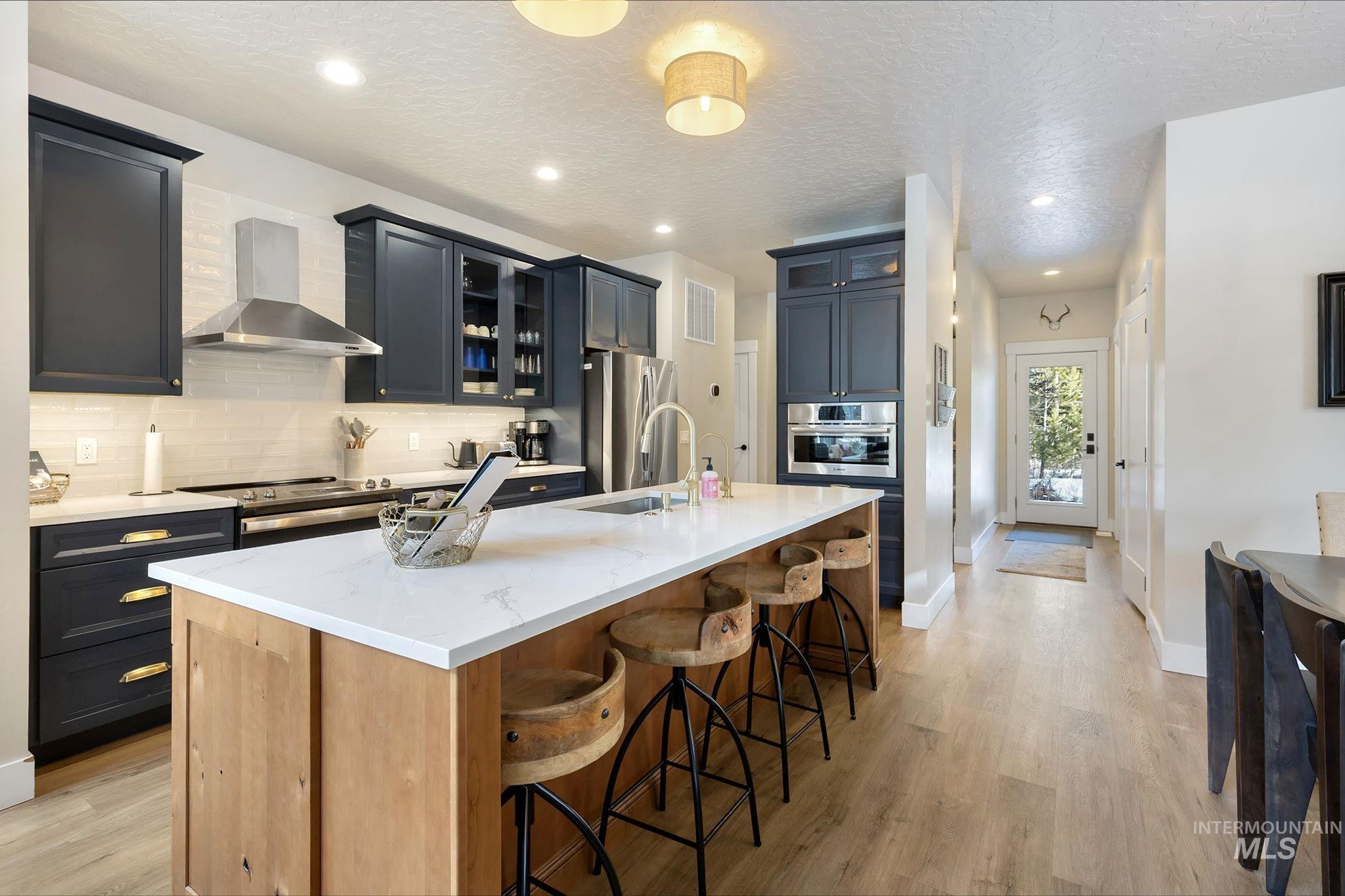 Kitchen with glass insert cabinets, light stone countertops, a large island with sink, a kitchen breakfast bar, and light wood-style flooring