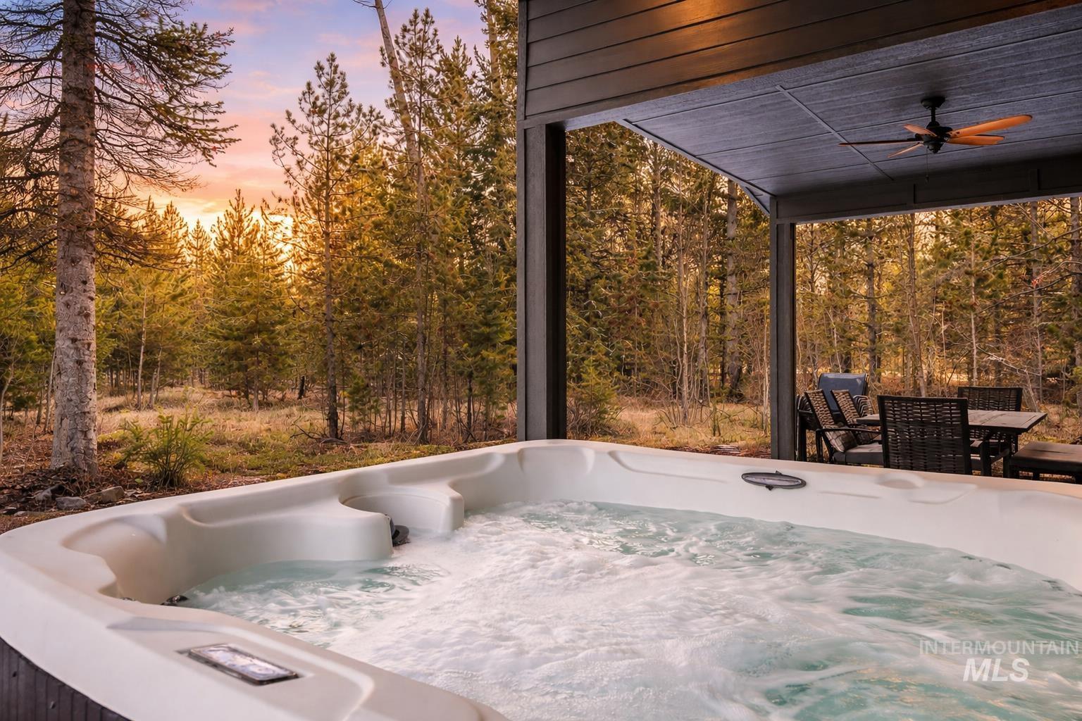 Patio terrace at dusk with ceiling fan, outdoor dining space, and a hot tub