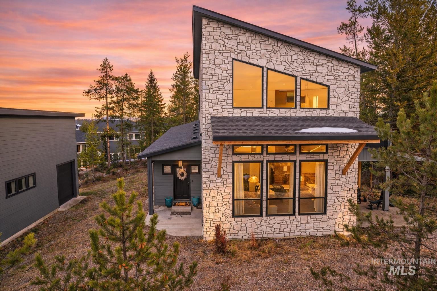 Back of property at dusk with stone siding and a shingled roof