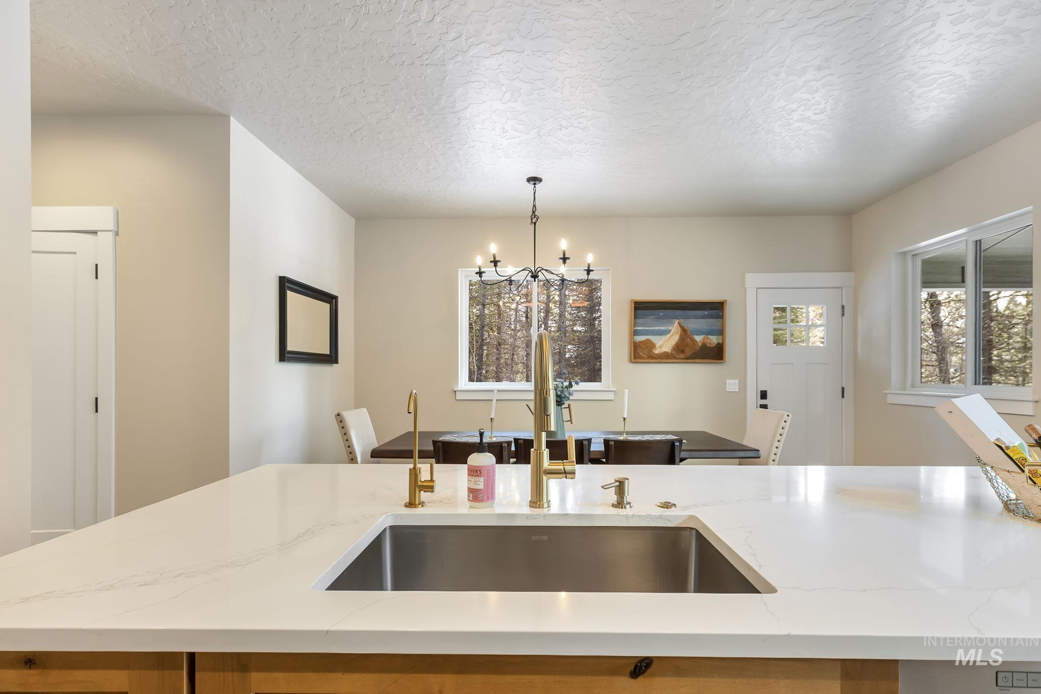 Kitchen with a textured ceiling, light stone countertops, hanging lights, and a center island with sink