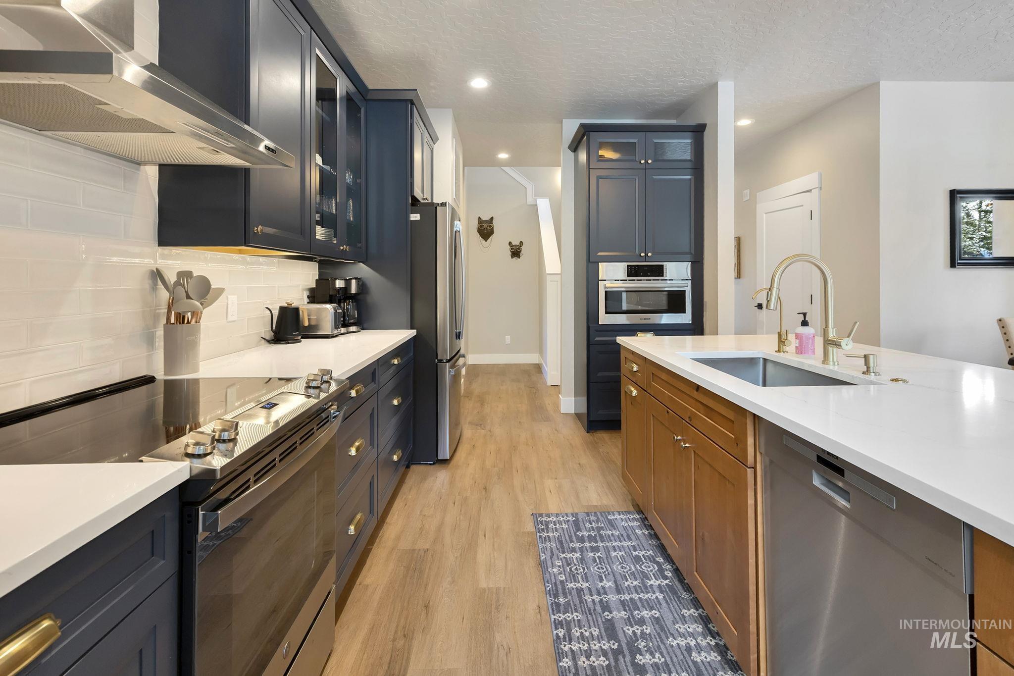 Kitchen with stainless steel appliances, glass insert cabinets, light wood finished floors, light stone countertops, and a textured ceiling