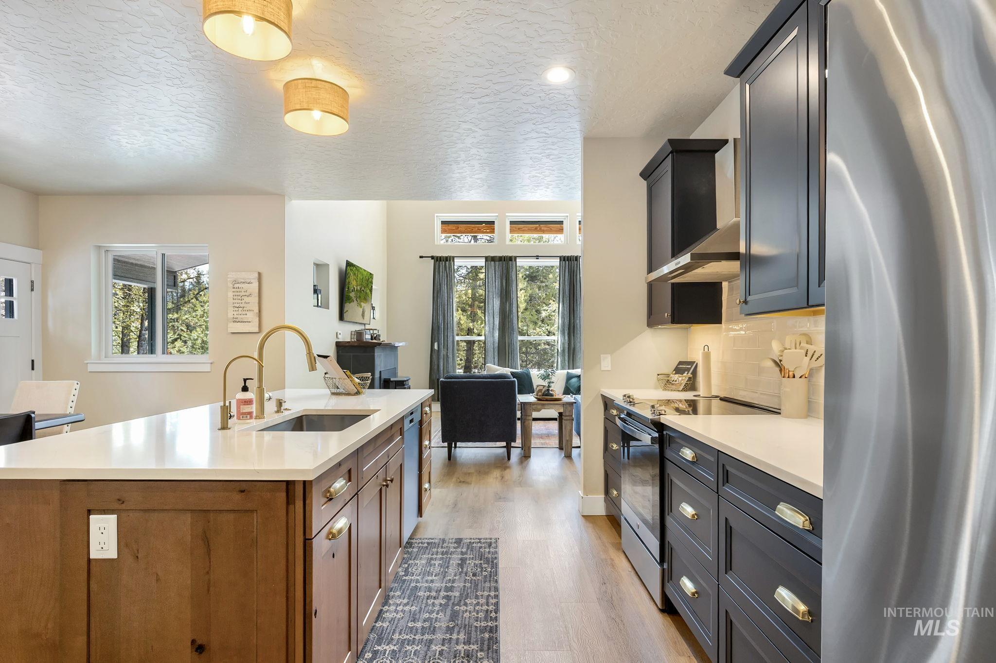 Kitchen featuring stainless steel appliances, light wood-style floors, light stone counters, a textured ceiling, and decorative backsplash