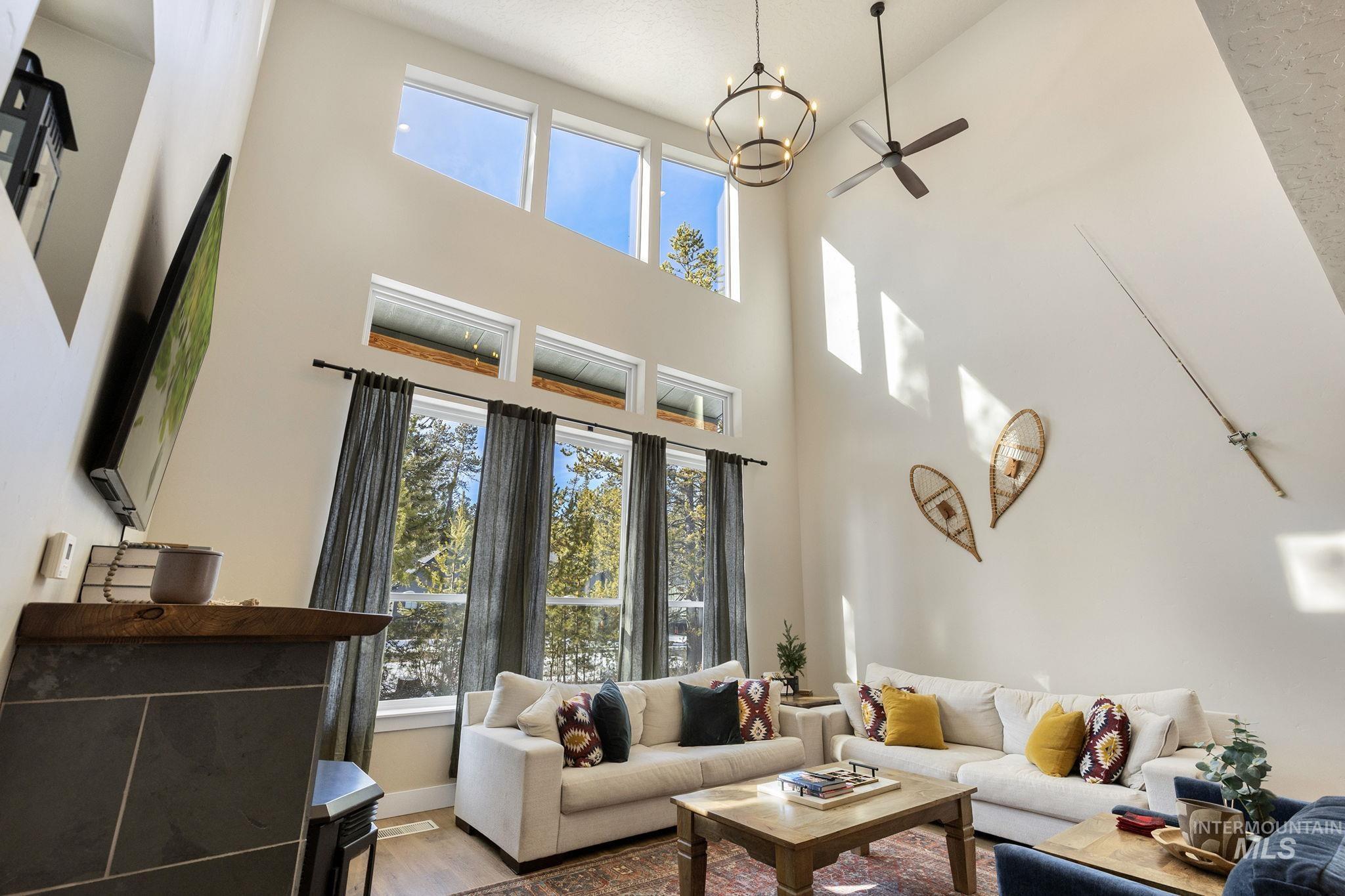 Living room featuring ceiling fan, wood finished floors, a chandelier, and a high ceiling