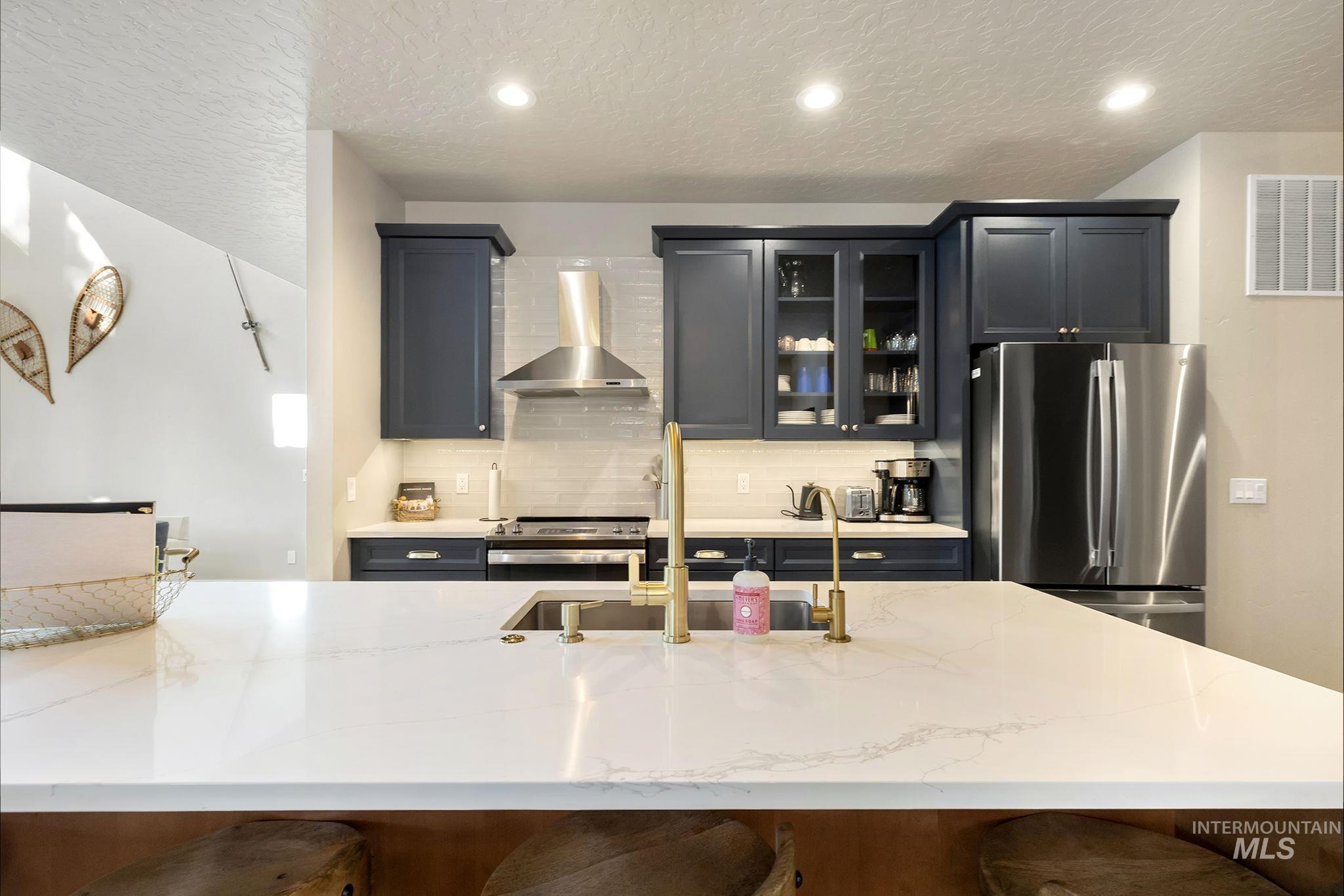Kitchen with glass fronted cabinets, stainless steel appliances, light stone countertops, decorative backsplash, and a breakfast bar area