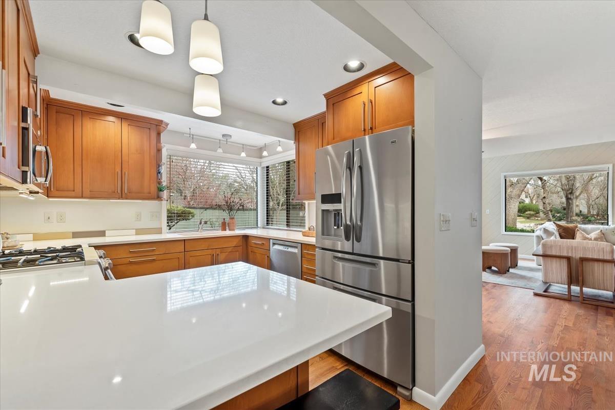Kitchen featuring appliances with stainless steel finishes, pendant lighting, light stone counters, a peninsula, and light wood finished floors