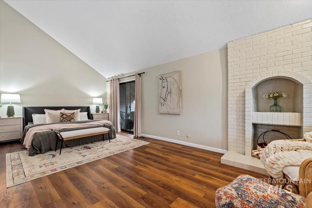 Bedroom featuring dark wood-style flooring, a brick fireplace, and high vaulted ceiling