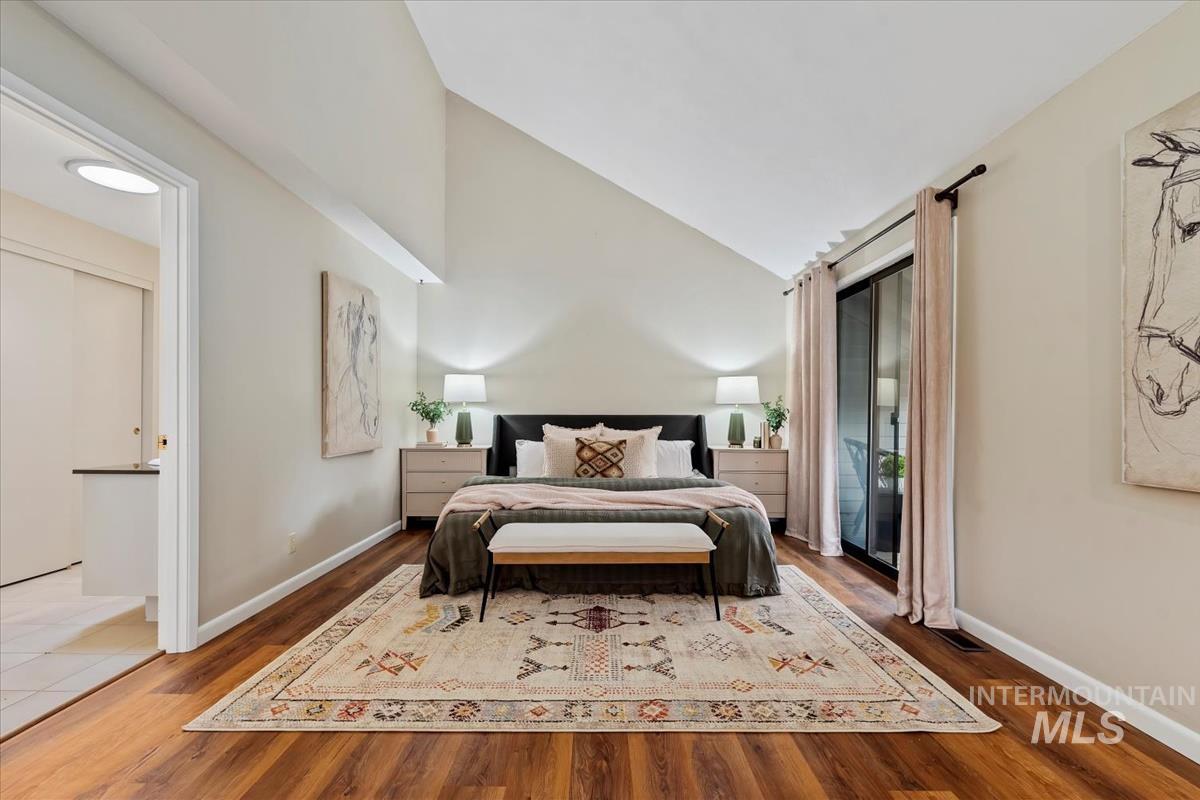 Bedroom with wood finished floors, access to exterior, and high vaulted ceiling