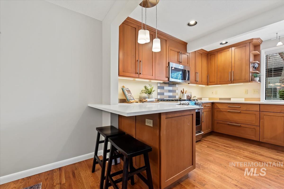 Kitchen with brown cabinets, a kitchen breakfast bar, light wood-style floors, stainless steel appliances, and recessed lighting