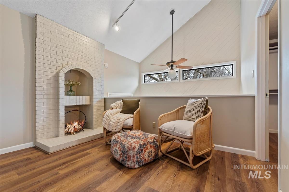 Living area with wood finished floors, a brick fireplace, high vaulted ceiling, and a ceiling fan