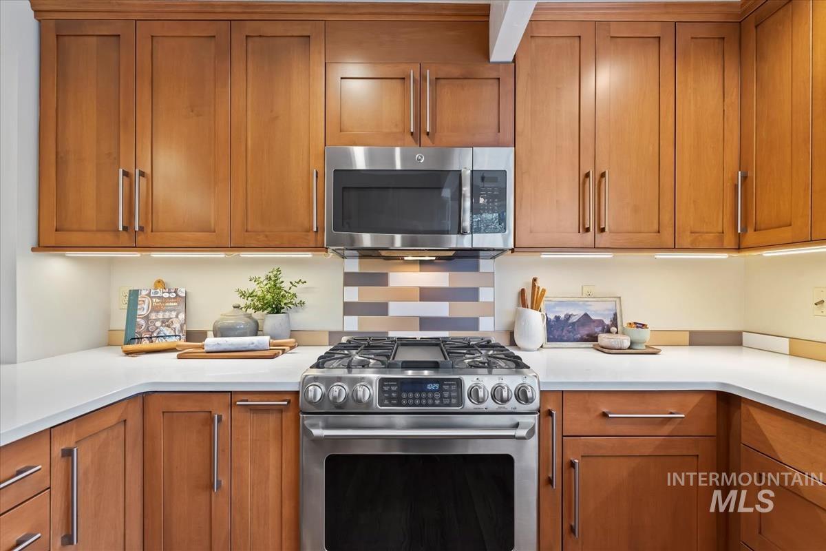 Kitchen with brown cabinetry, stainless steel appliances, tasteful backsplash, and light stone counters