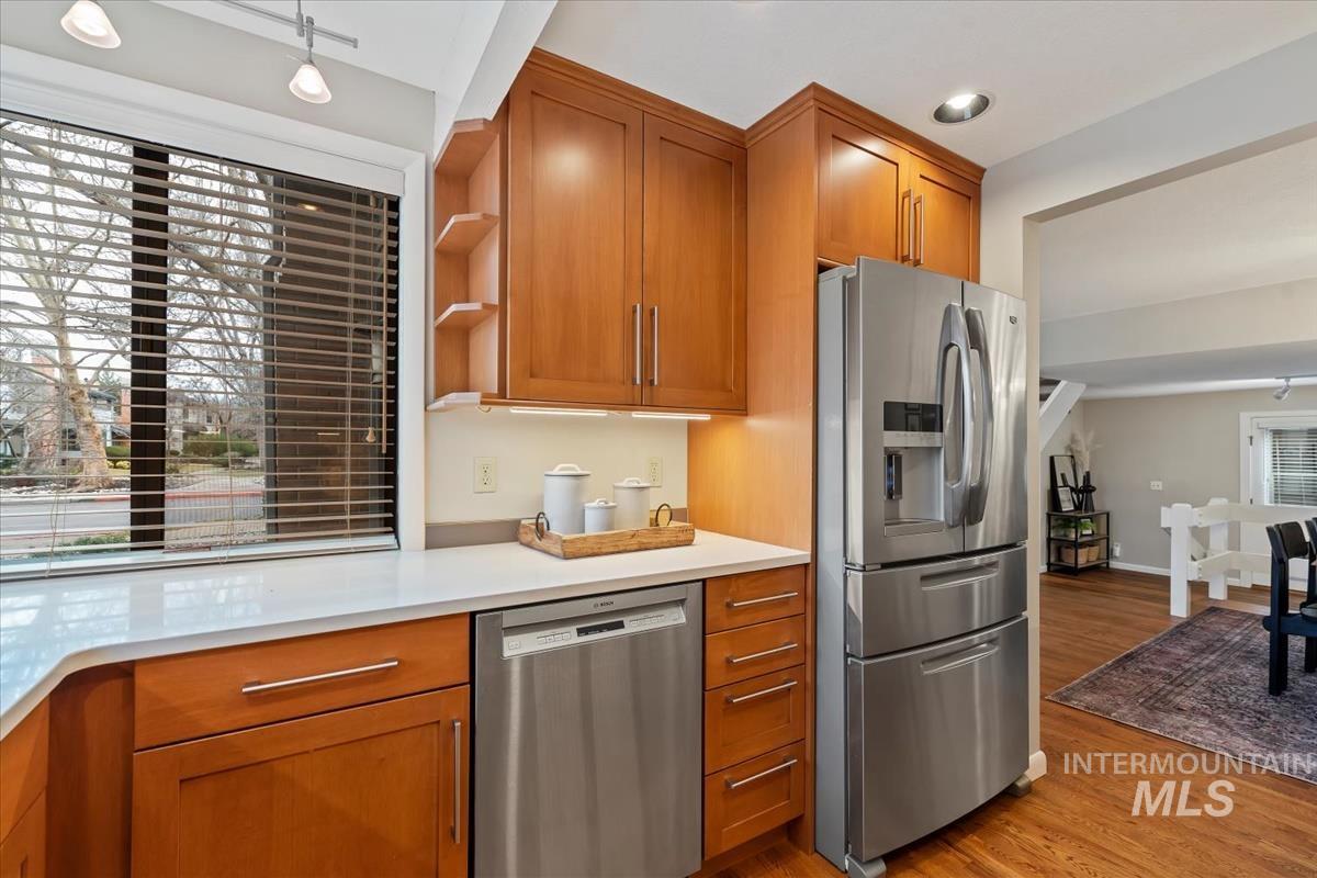 Kitchen with open shelves, appliances with stainless steel finishes, brown cabinetry, light wood-type flooring, and light stone countertops