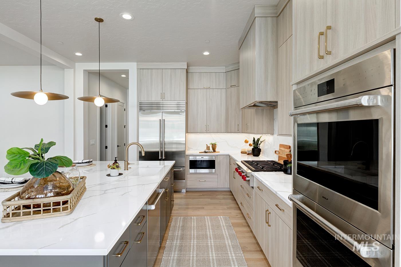 Kitchen featuring appliances with stainless steel finishes, pendant lighting, light wood-style floors, light stone counters, and a textured ceiling