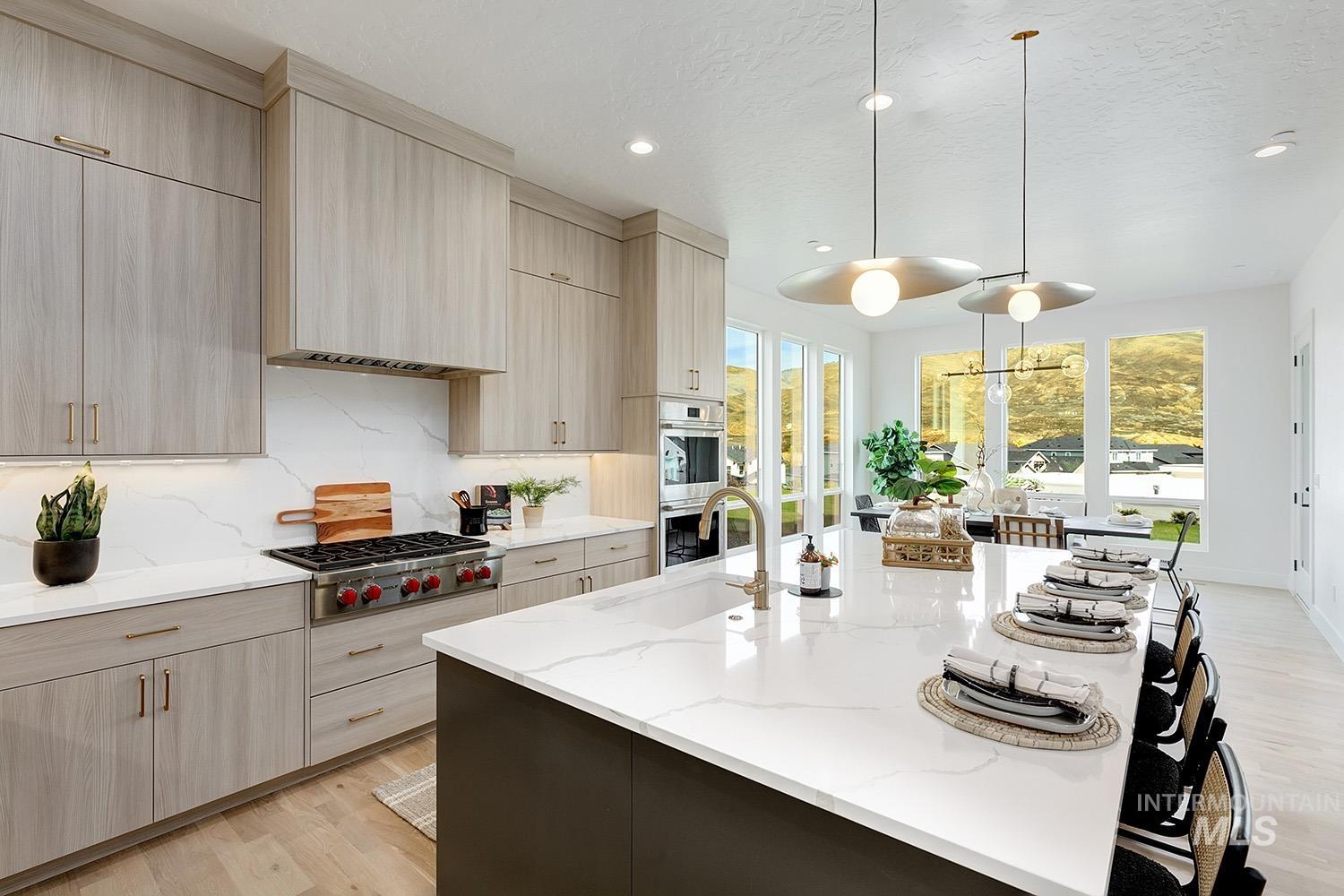 Kitchen with decorative light fixtures, light brown cabinetry, light wood finished floors, light stone countertops, and backsplash