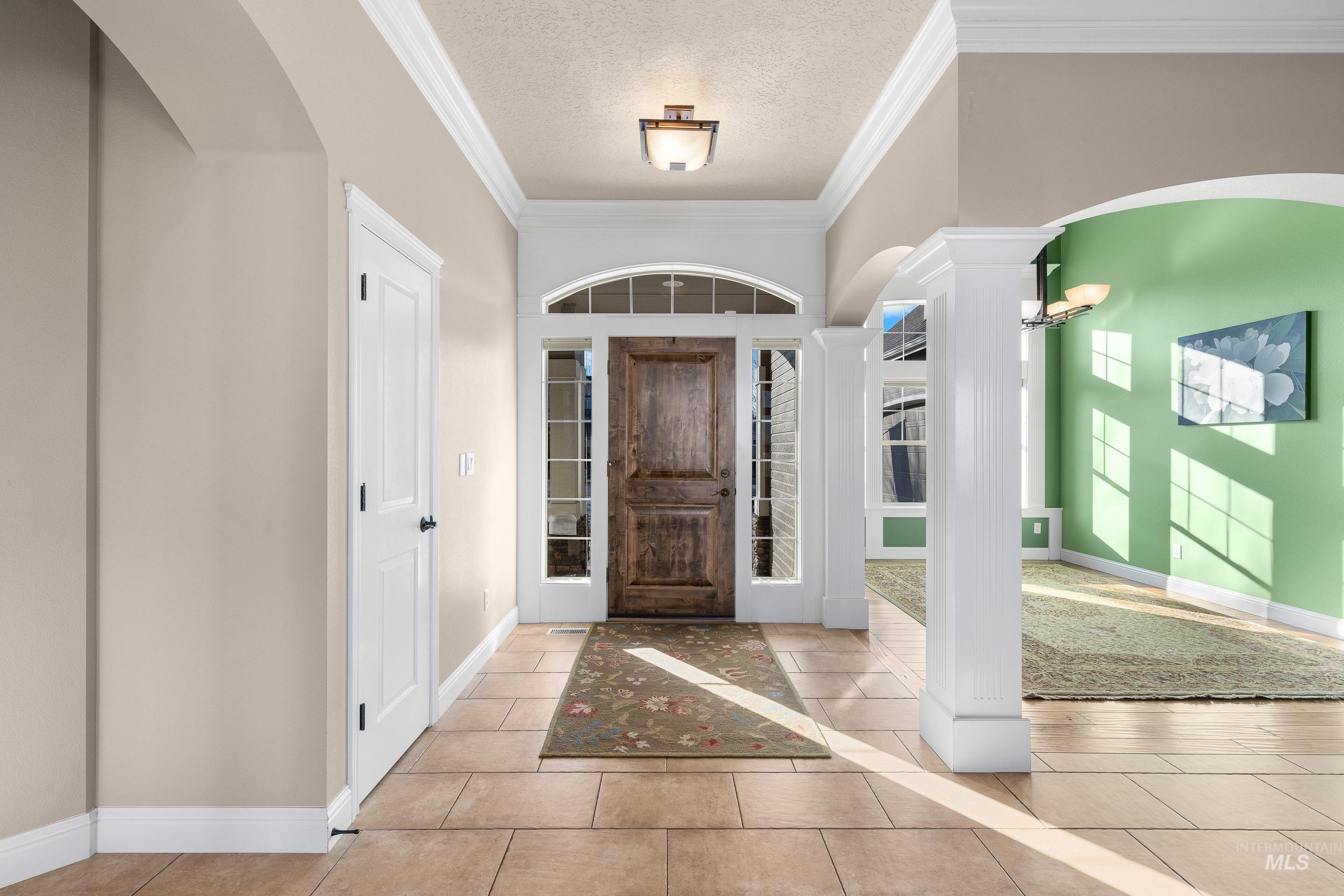 Foyer with arched walkways, a textured ceiling, ornamental molding, and light tile patterned flooring
