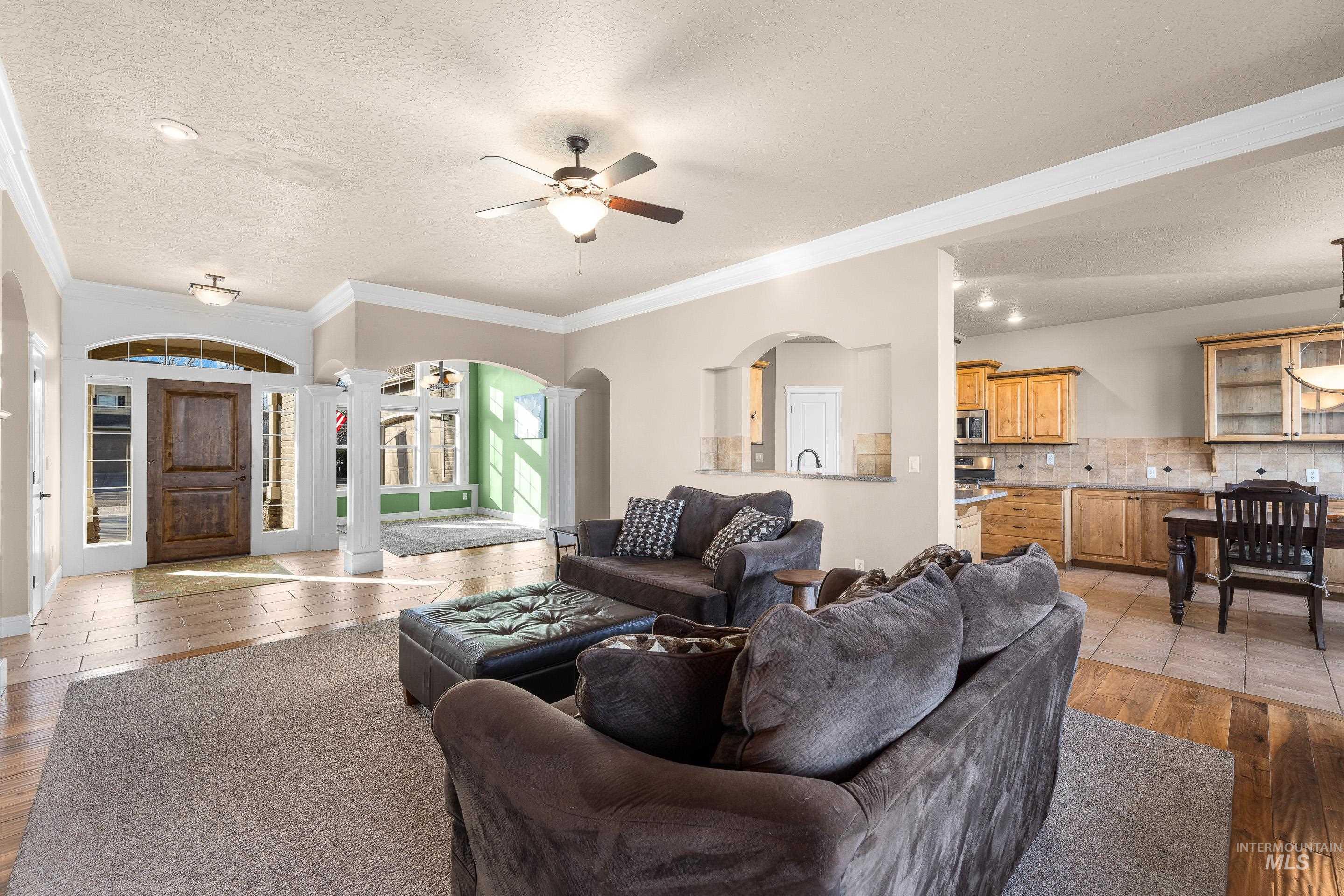 Living room featuring light wood-type flooring, a textured ceiling, crown molding, ceiling fan, and ornate columns