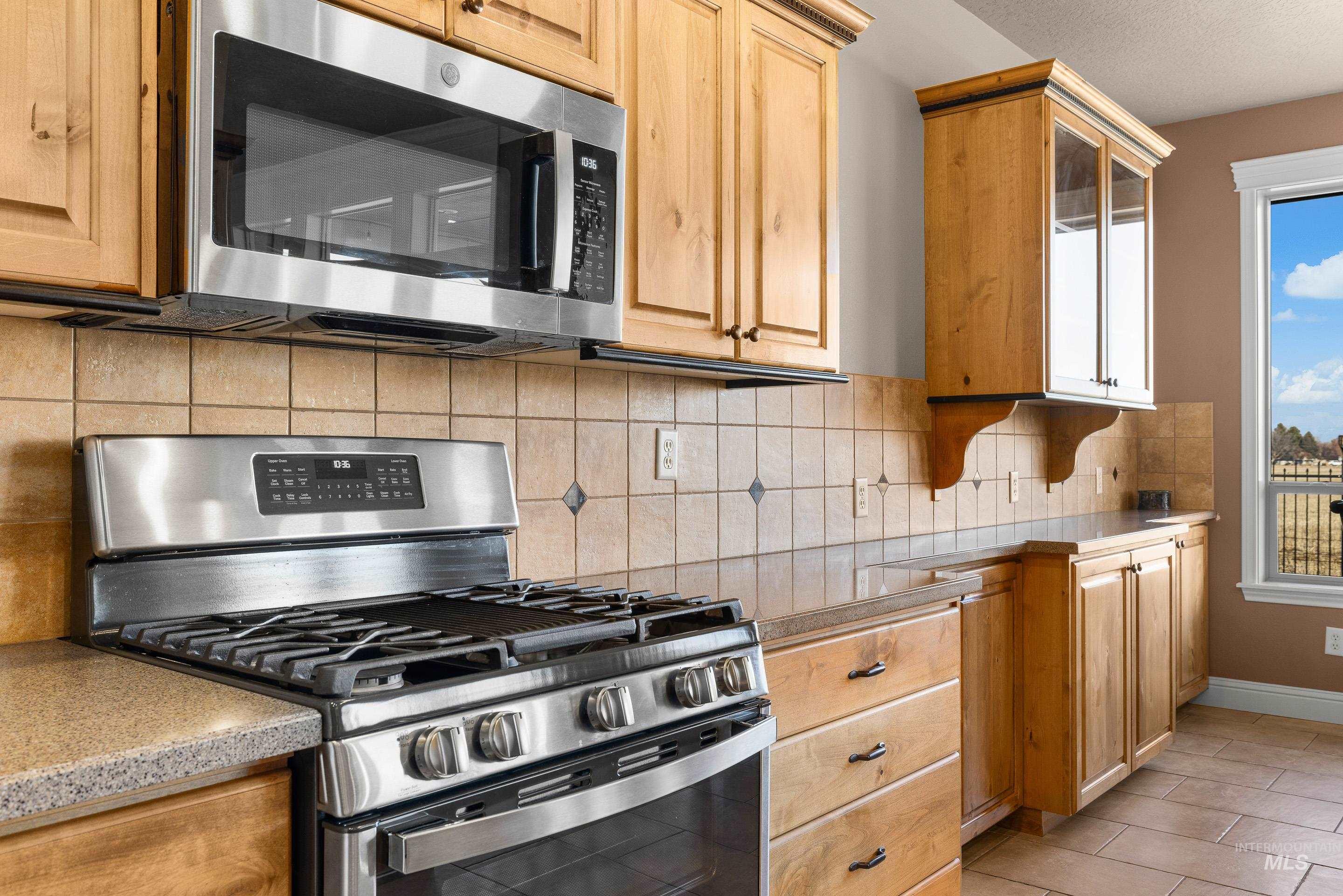 Kitchen with appliances with stainless steel finishes, backsplash, glass insert cabinets, and light tile patterned floors
