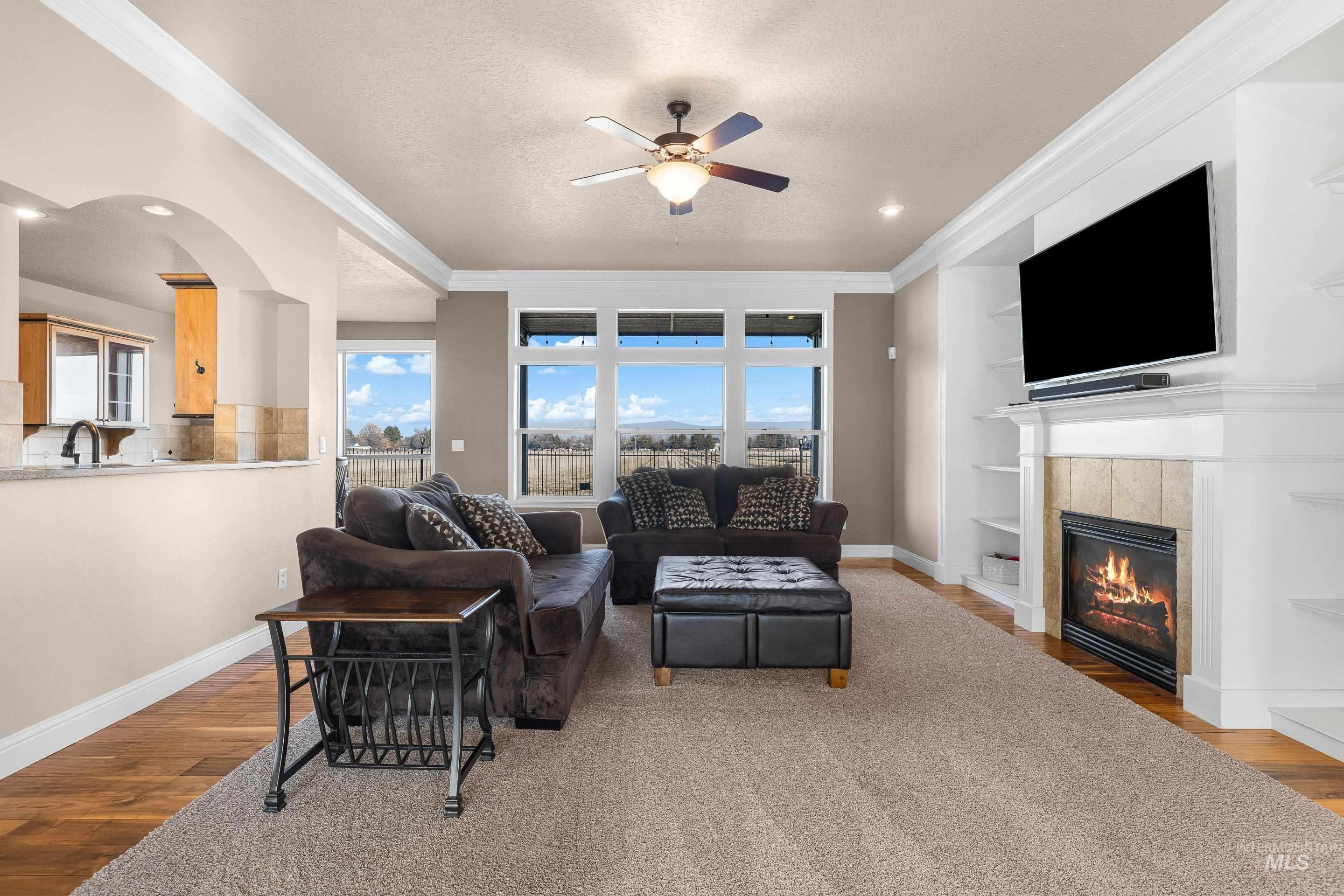 Living area featuring built in features, light wood-style flooring, crown molding, a fireplace, and plenty of natural light