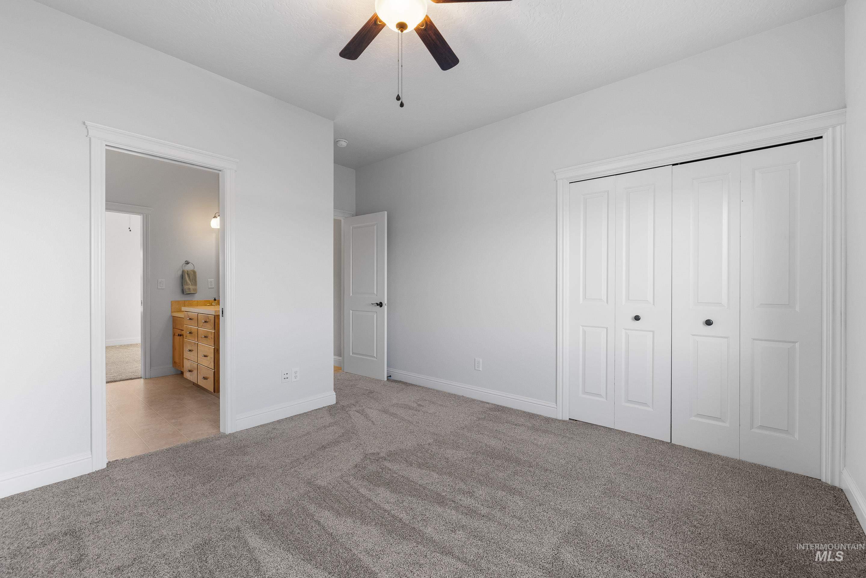 Unfurnished bedroom featuring light colored carpet, a closet, ceiling fan, and ensuite bath