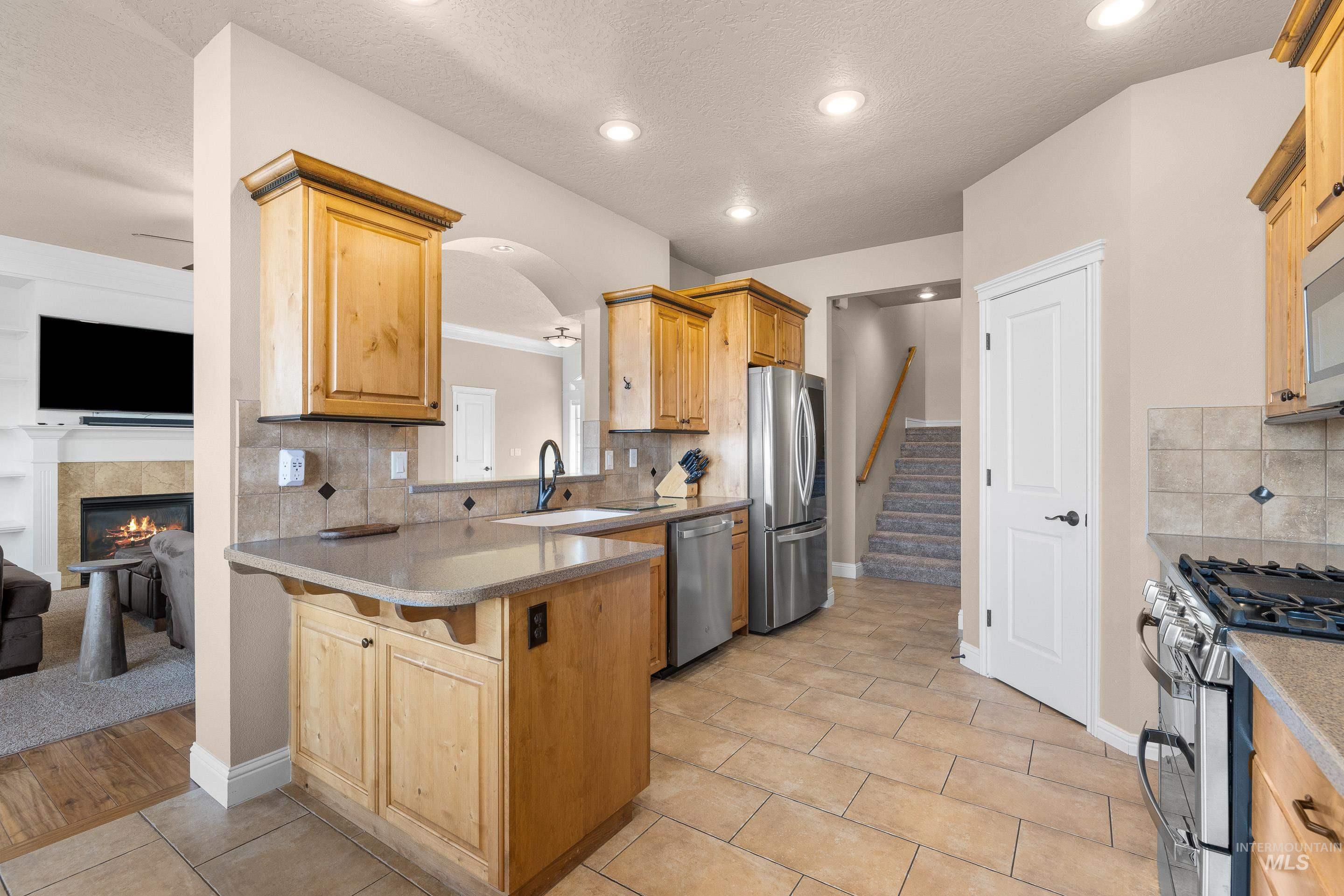 Kitchen featuring decorative backsplash, appliances with stainless steel finishes, a tile fireplace, arched walkways, and light tile patterned floors