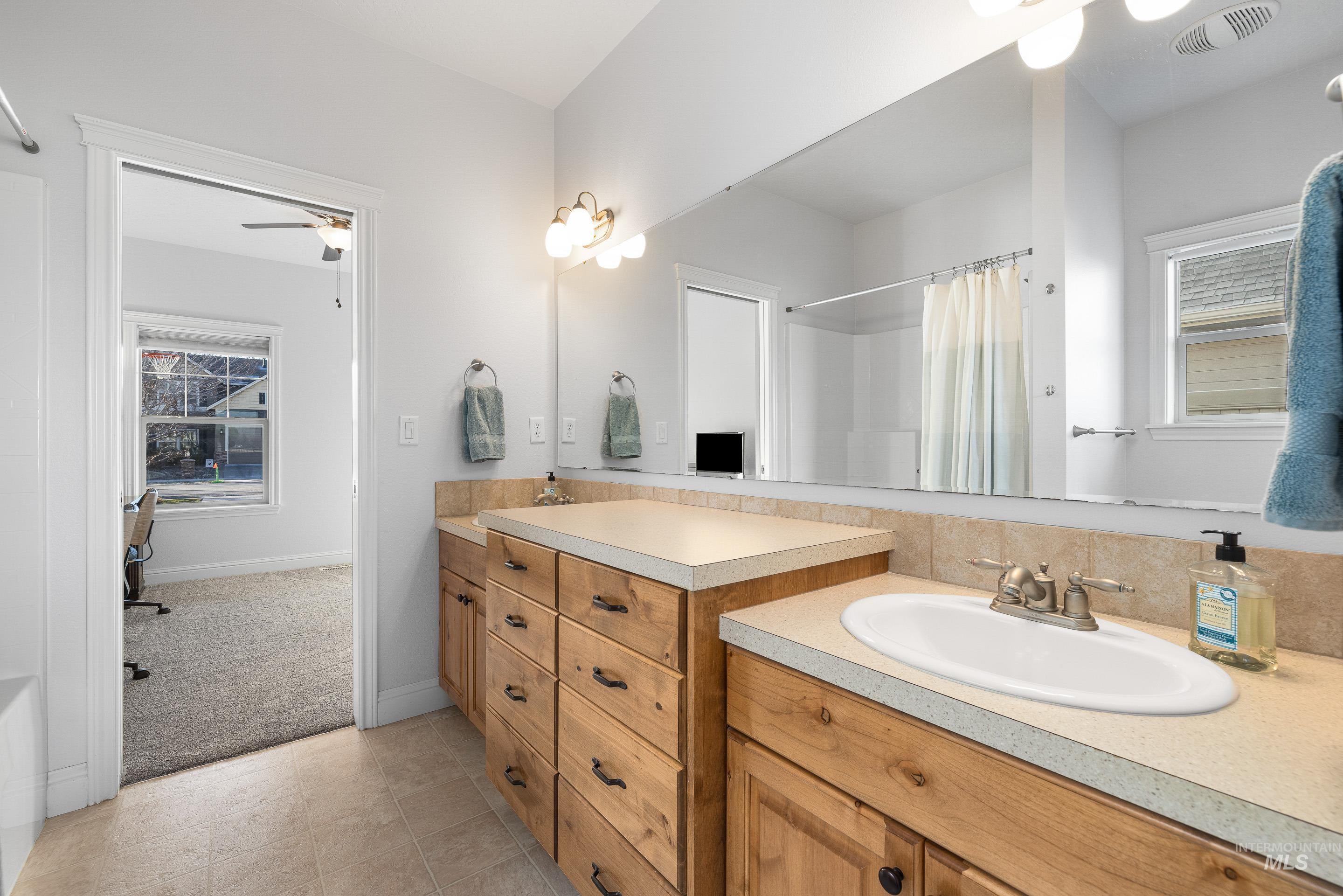 Full bath featuring double vanity, a shower with curtain, light tile patterned floors, and a ceiling fan