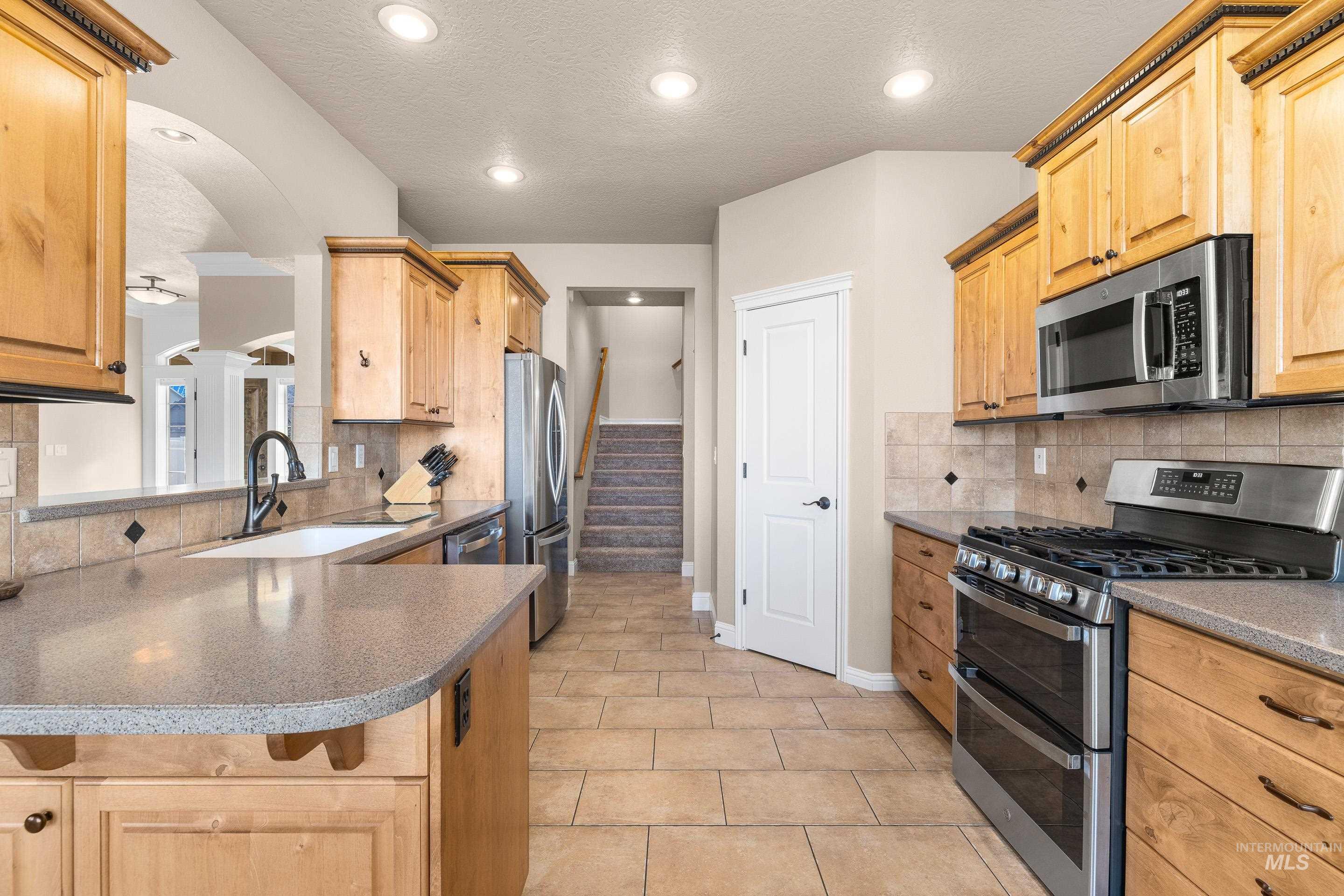 Kitchen with stainless steel appliances, arched walkways, light brown cabinets, light tile patterned floors, and backsplash